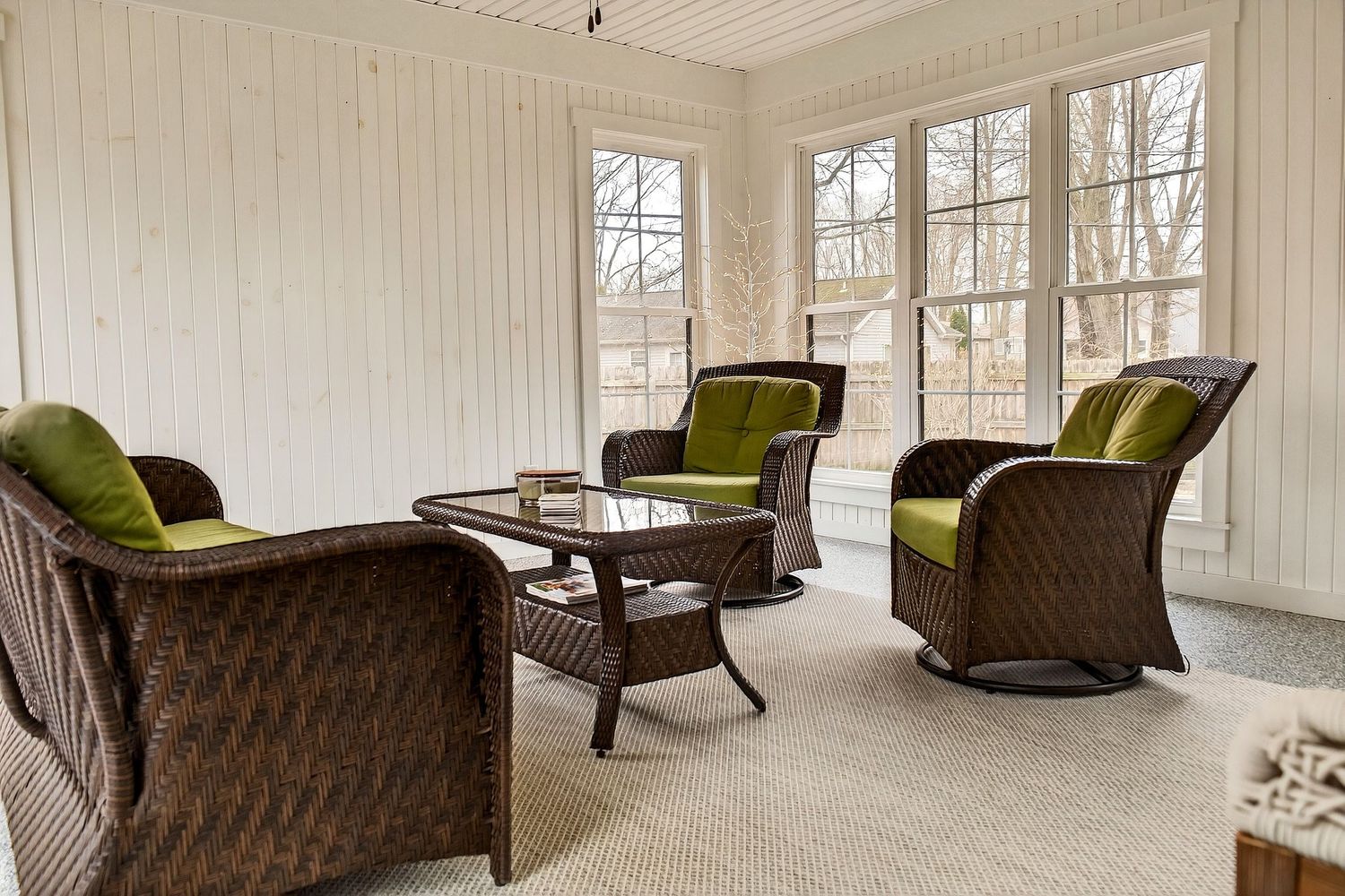 Elegant sunroom with white walls features brown wicker furniture and olive green cushions in a bright, airy space.