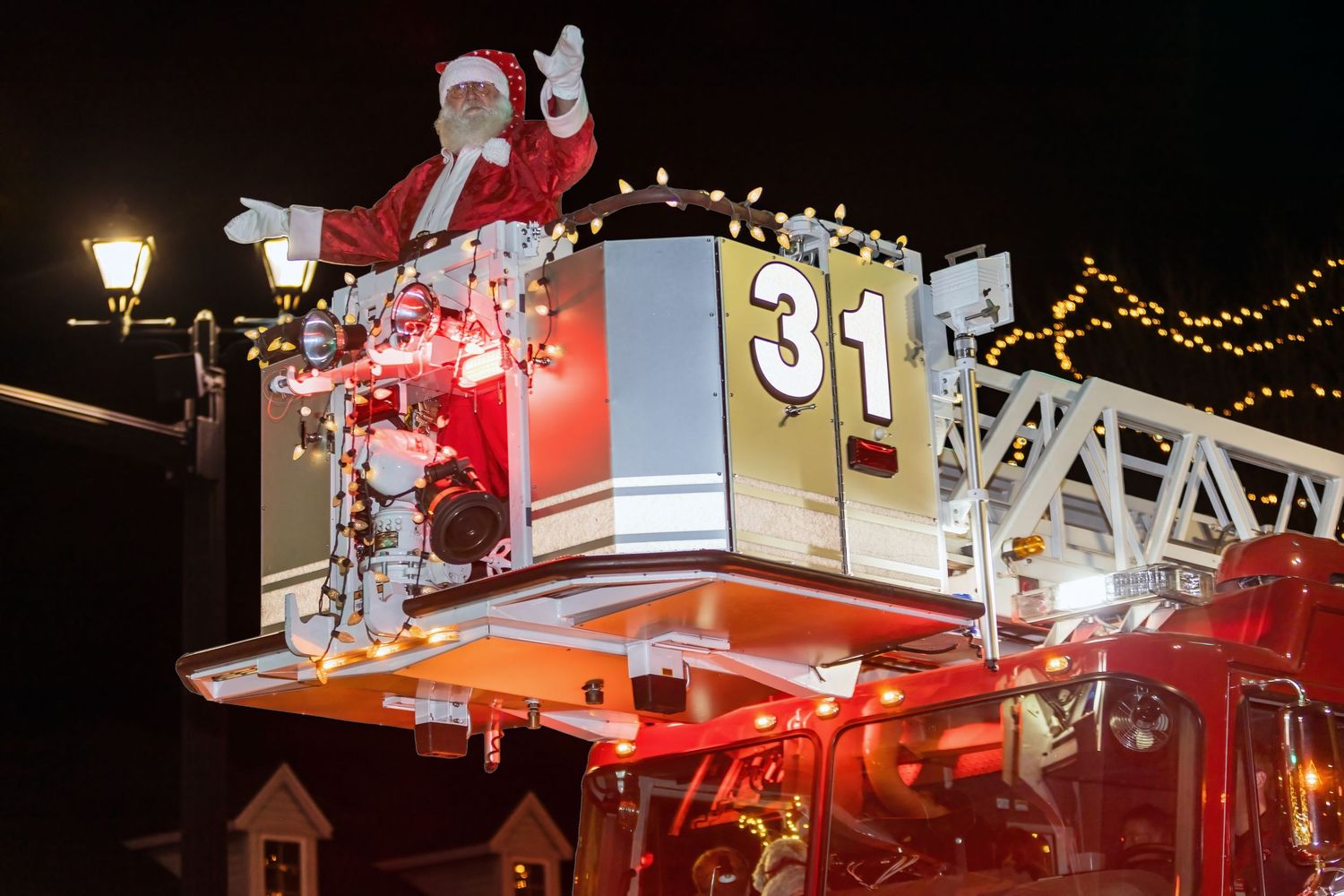 Santa Claus riding on a decorated holiday float at night with festive lights.