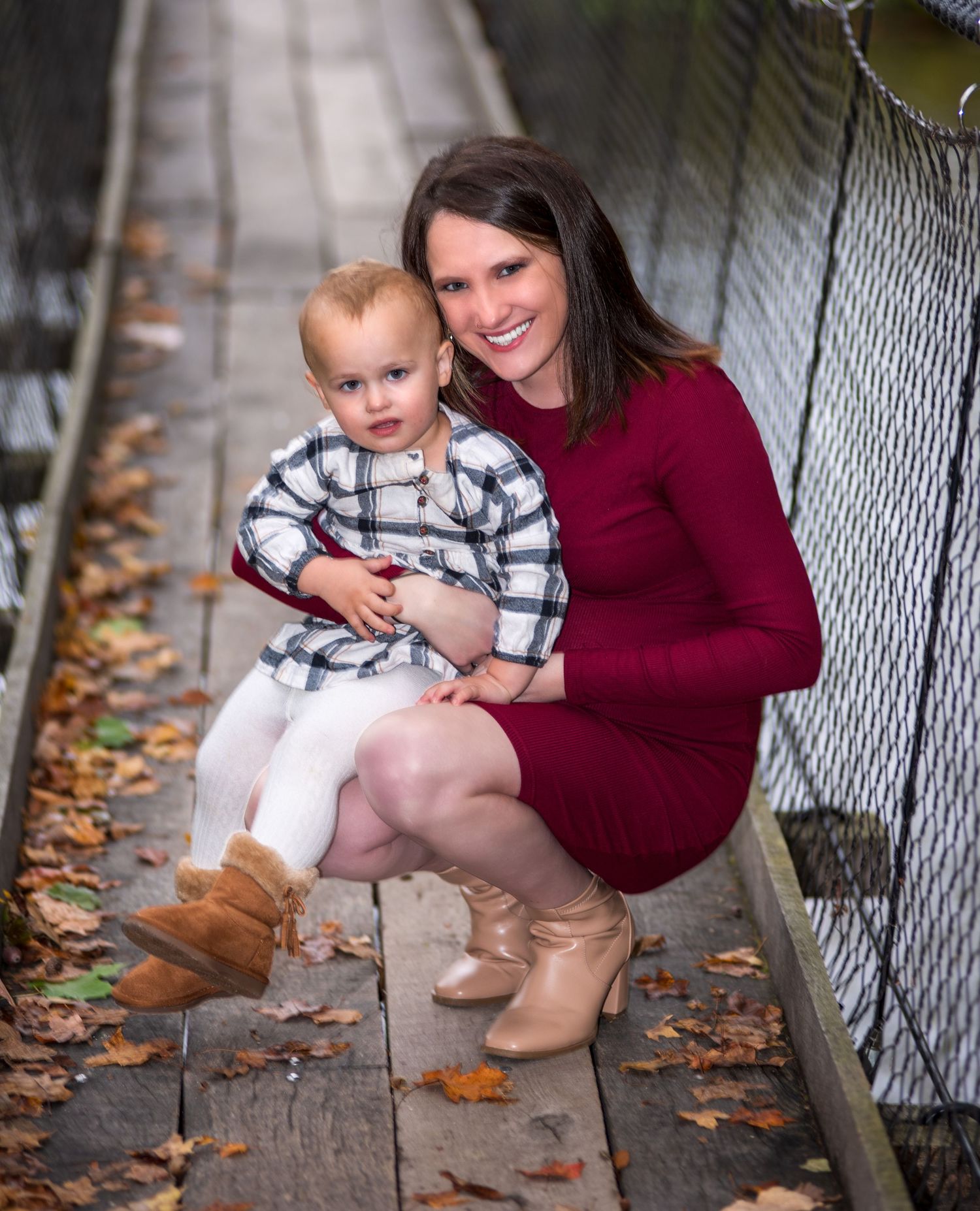 Family photoshoot on wooden bridge with autumn leaves and plaid clothing.