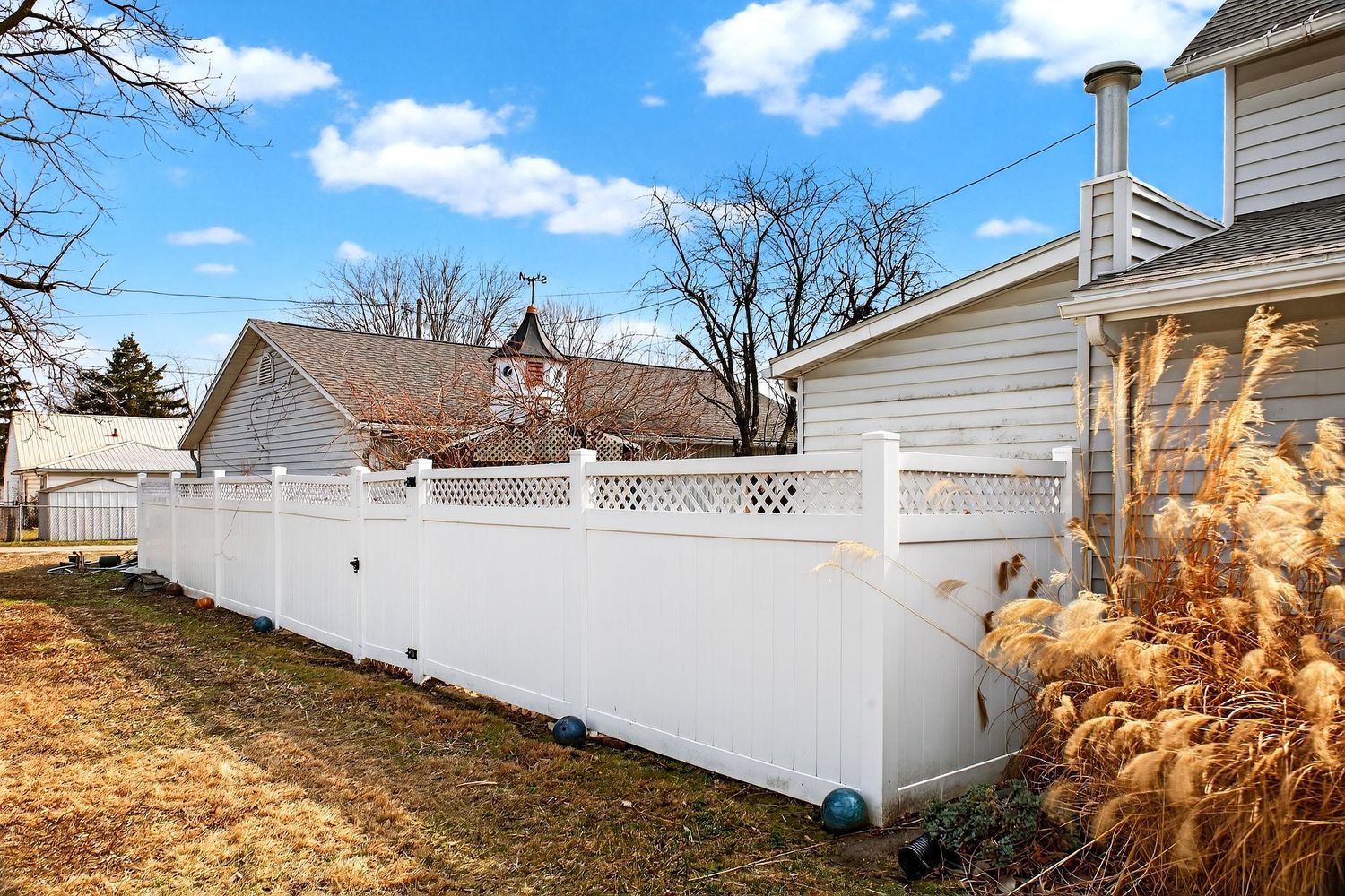 White vinyl privacy fence installation along a residential backyard property line during winter season.