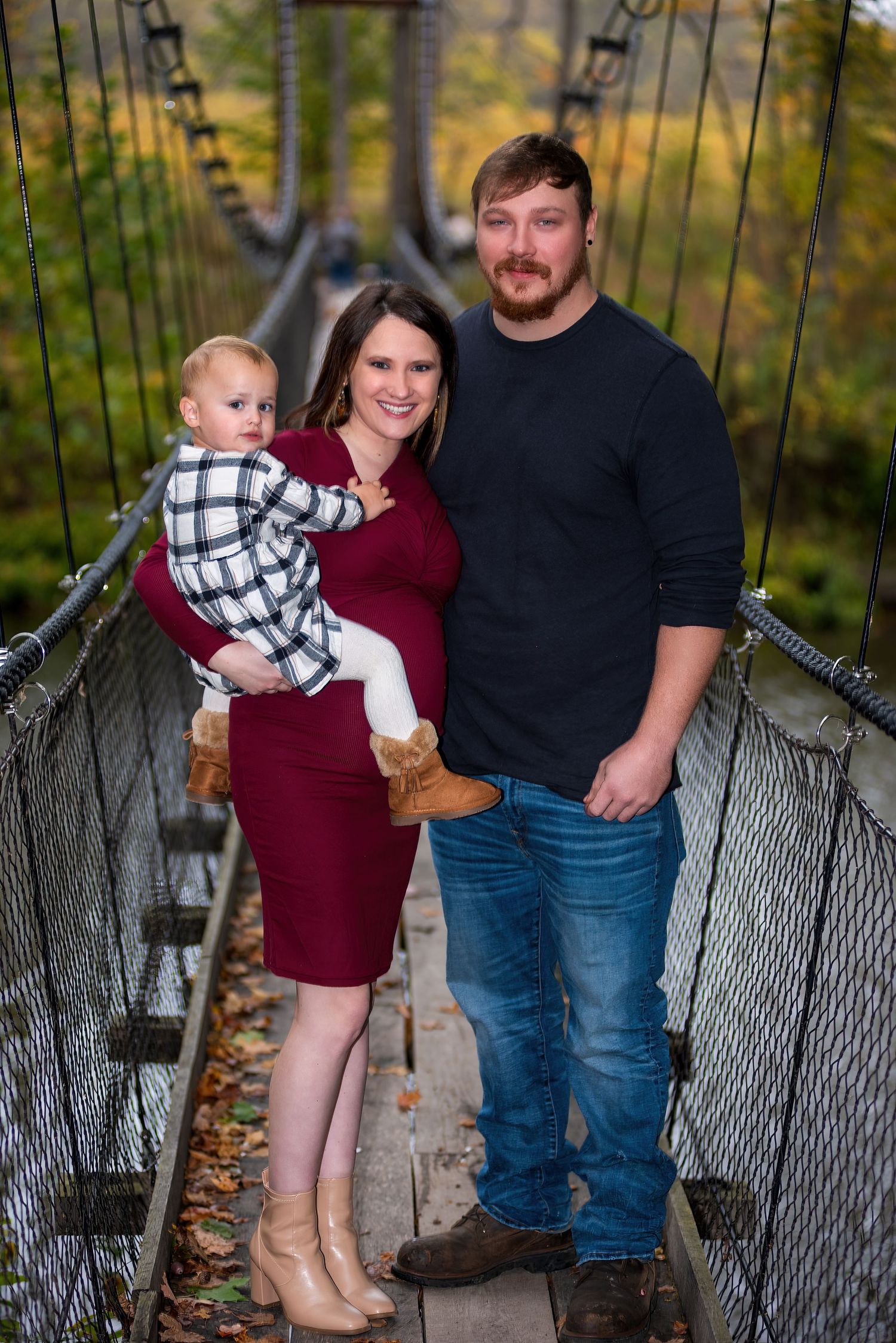 Family portrait on wooden bridge surrounded by fall foliage.