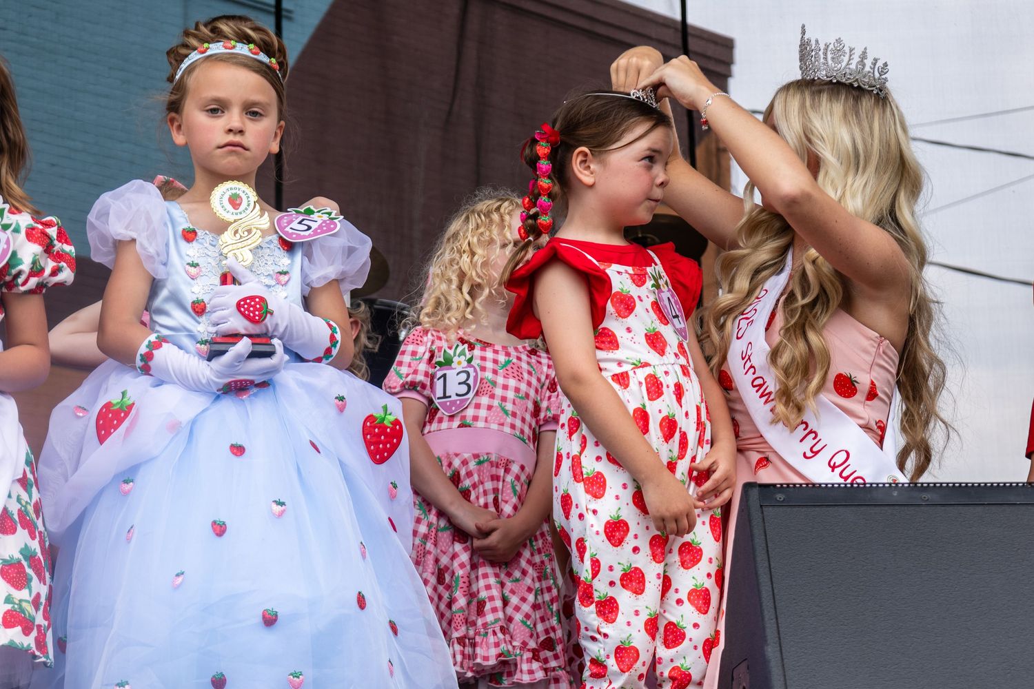 Group wearing strawberry-themed outfits posing together on an outdoor stage.