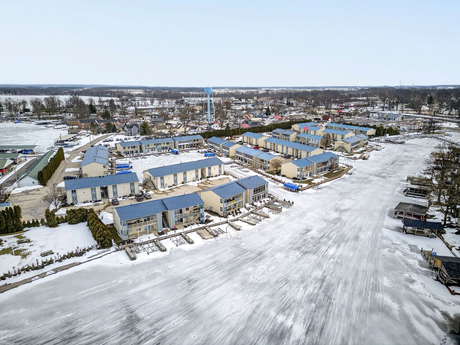 Aerial winter view of waterfront condominiums and marina with snow covered ground in coastal New England town.