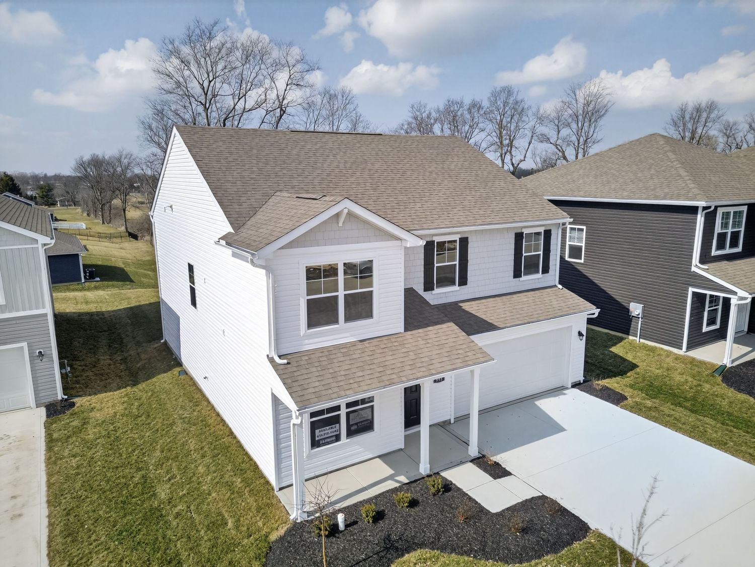 Aerial view of white residential homes with gray roofs and green lawns in a suburban neighborhood.
