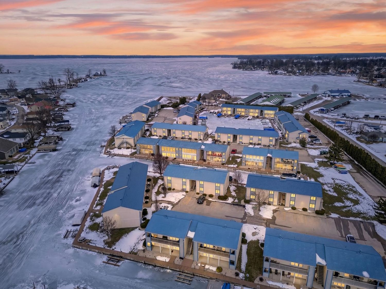 Aerial view of snow-covered industrial buildings with warm sunset sky reflecting off their rooftops.