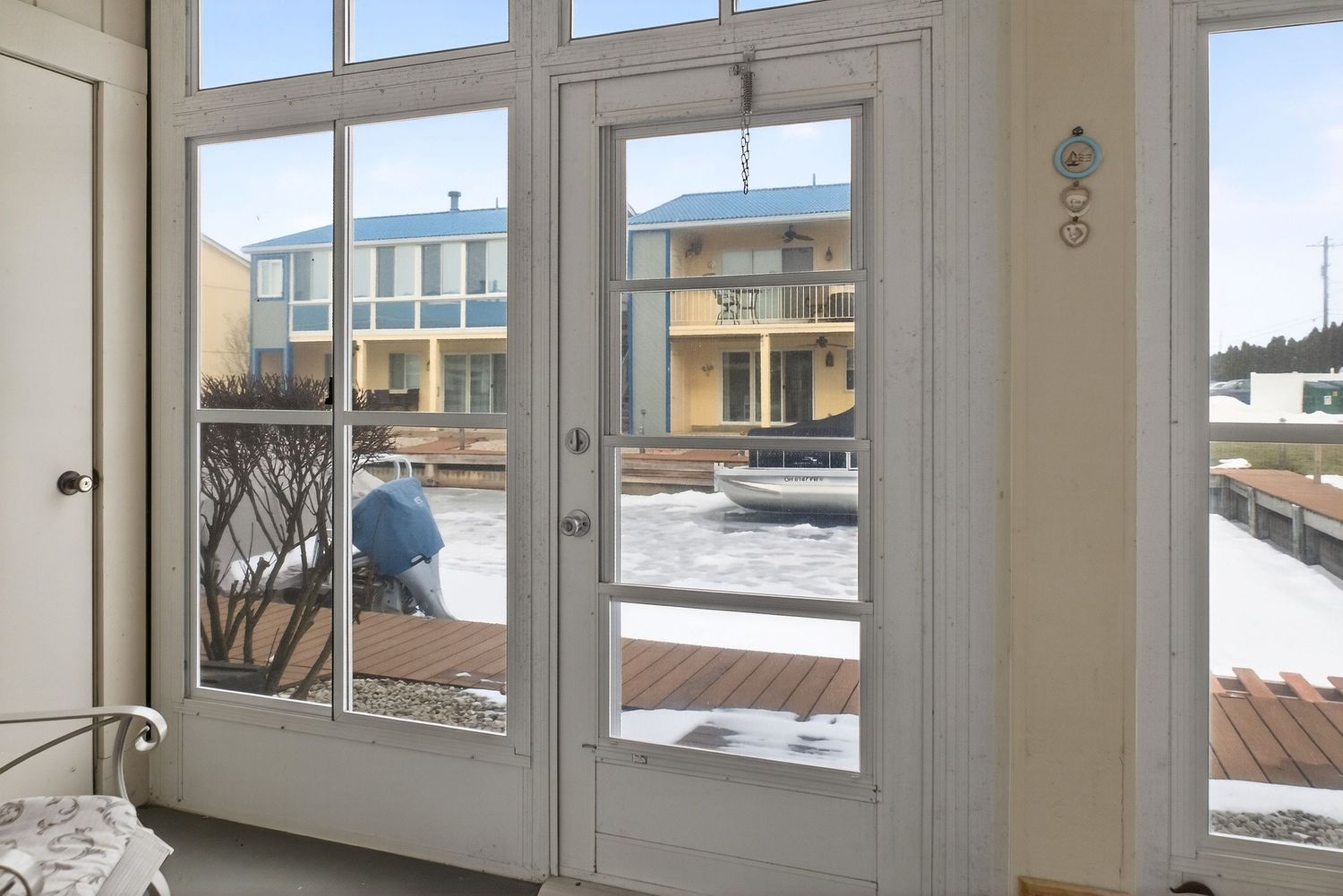 Glass double doors in white frame looking out onto a snowy wooden deck with residential buildings visible in background.