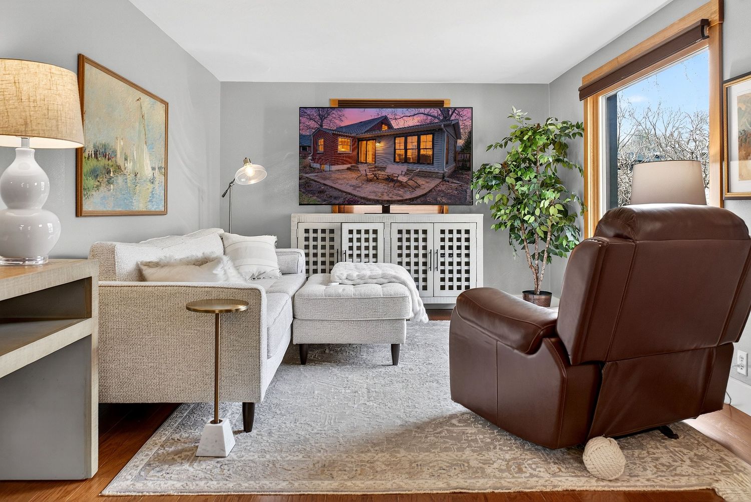 Modern living room features white walls, brown leather furniture, and natural light from large windows.