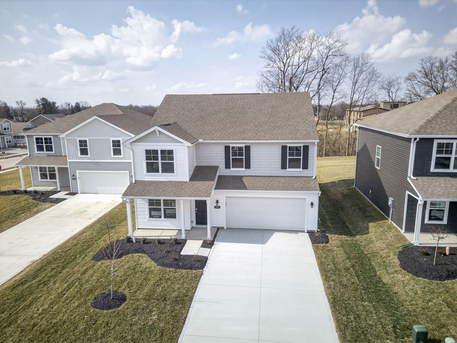 Aerial view of modern two-story suburban house with attached garage and white driveway on green lawn under blue sky.