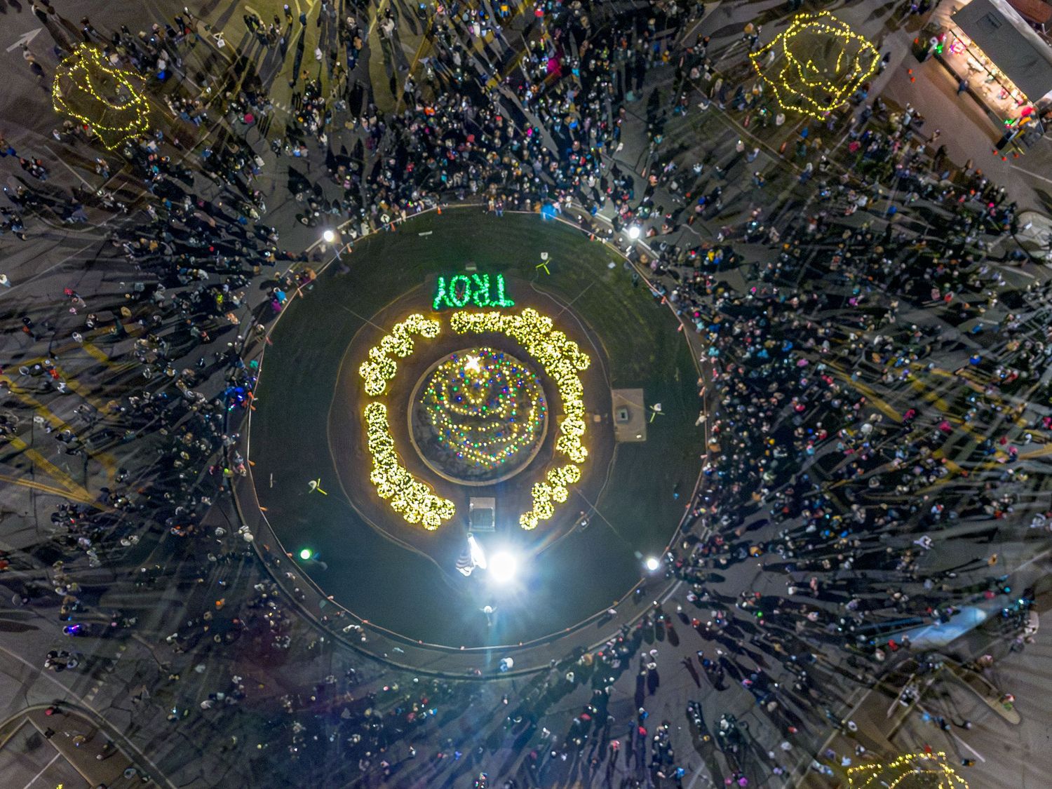 Aerial view of a large circular holiday light display with crowds gathering in a spiral pattern.