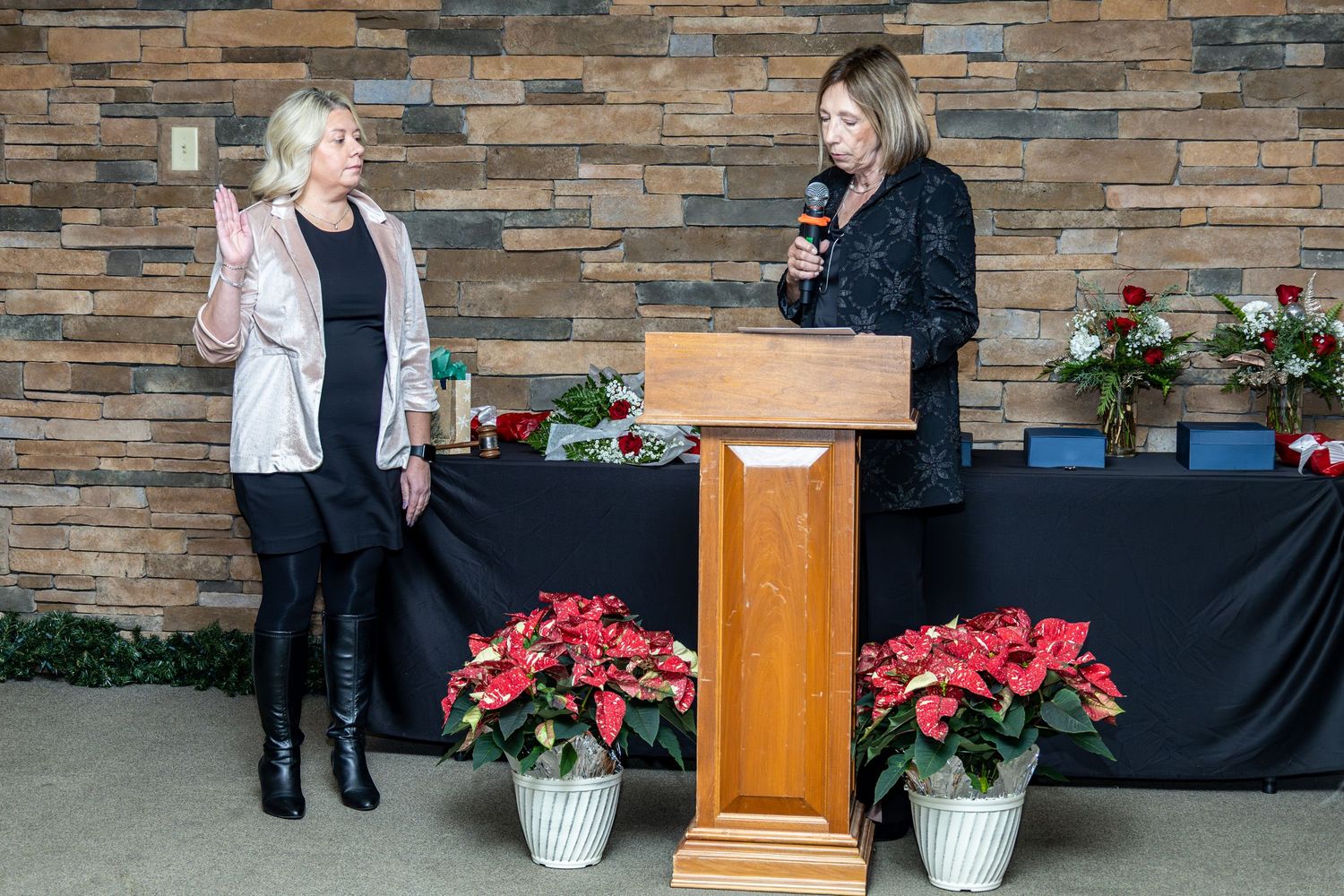 Festive decorative poinsettia plants flank a wooden podium against a stone brick wall.