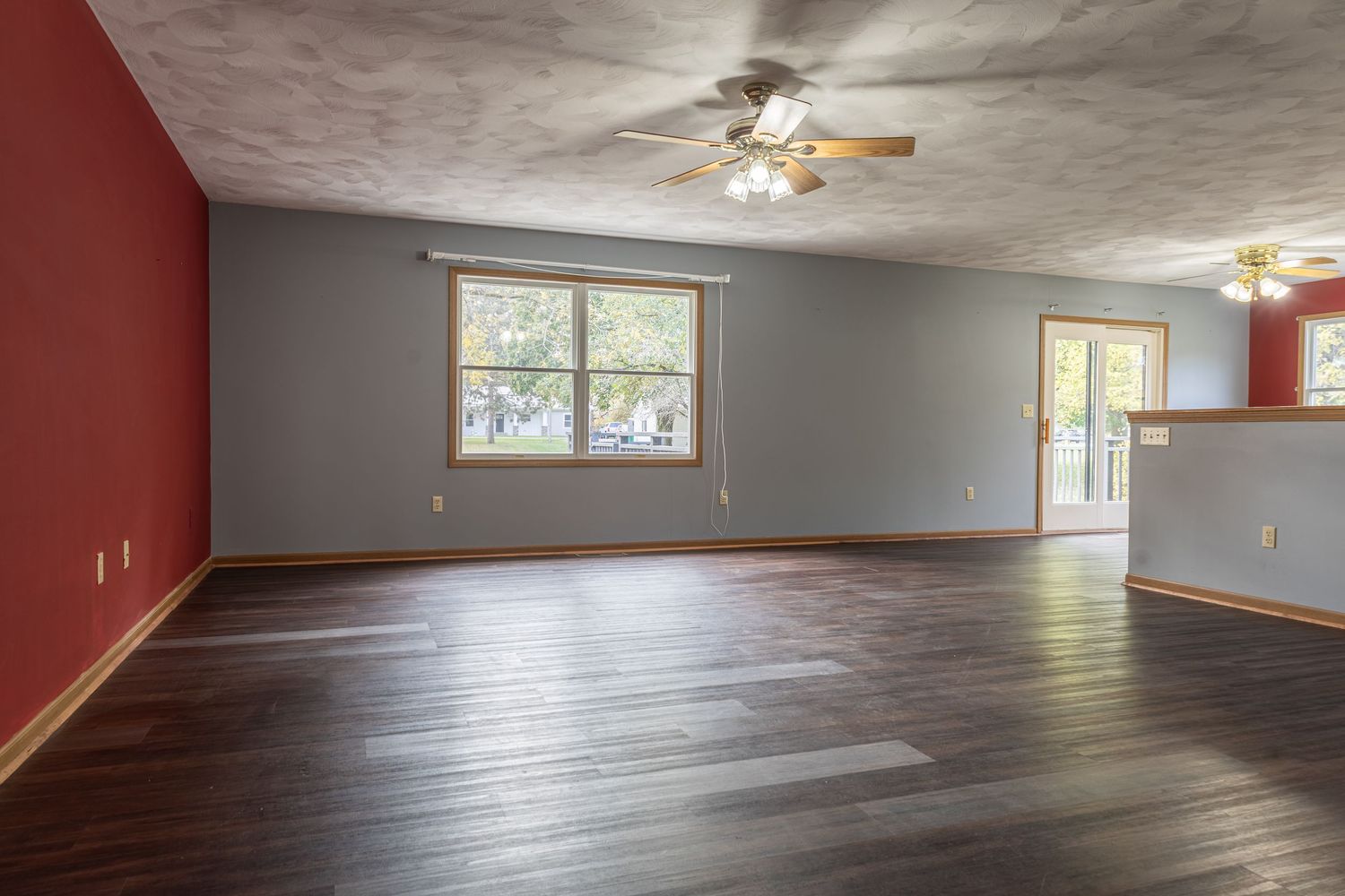 Spacious empty room with gray walls, ceiling fan, and large windows letting in natural light.