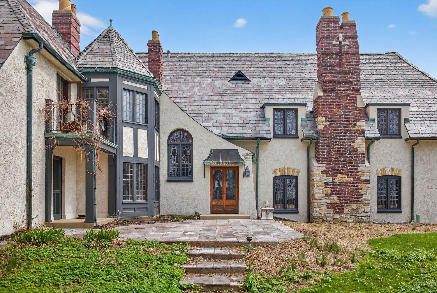 Exterior view of a Tudor-style home with multiple brick chimneys, arched doorways and traditional architectural details.