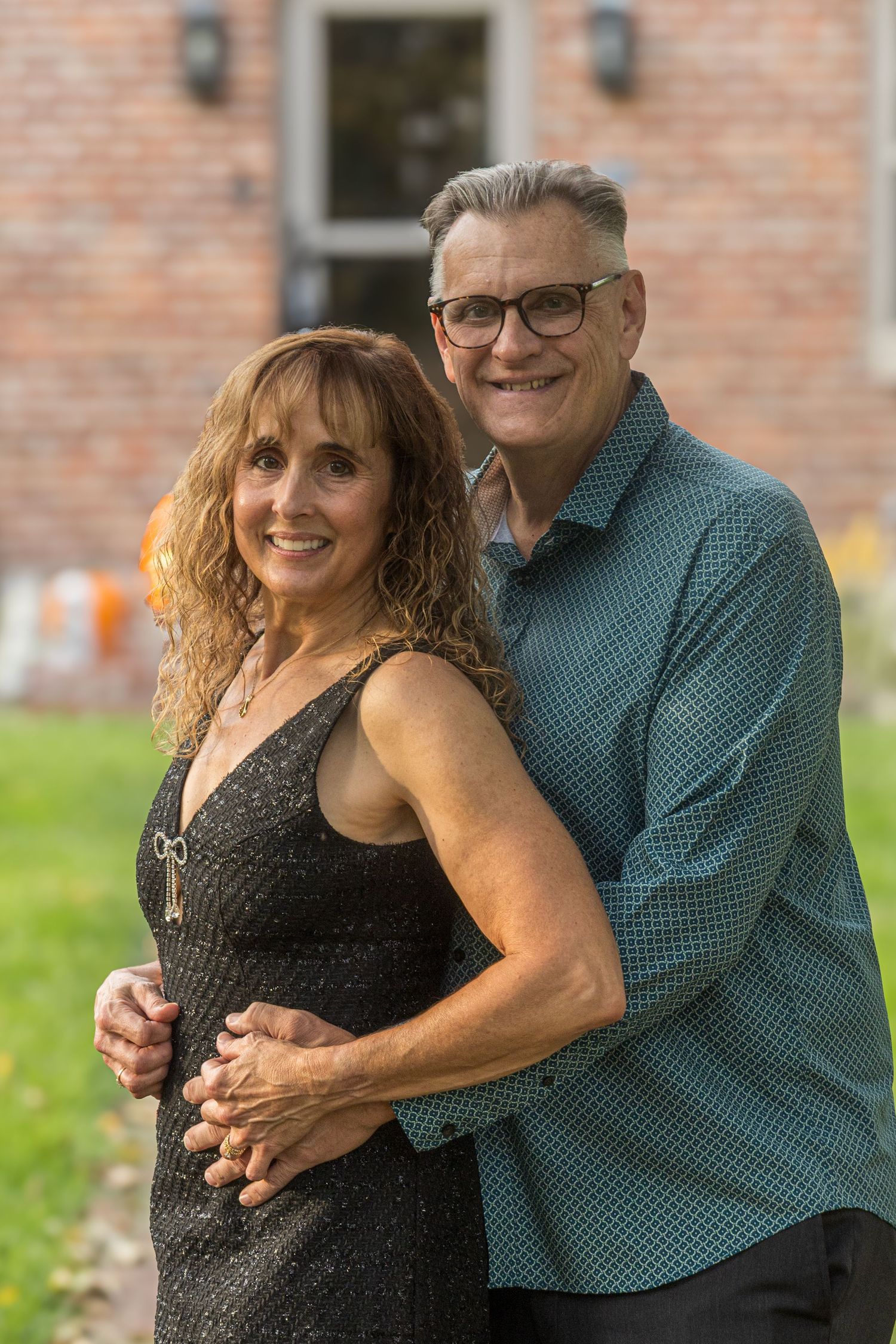Couple embracing outdoors against brick wall background at sunset.