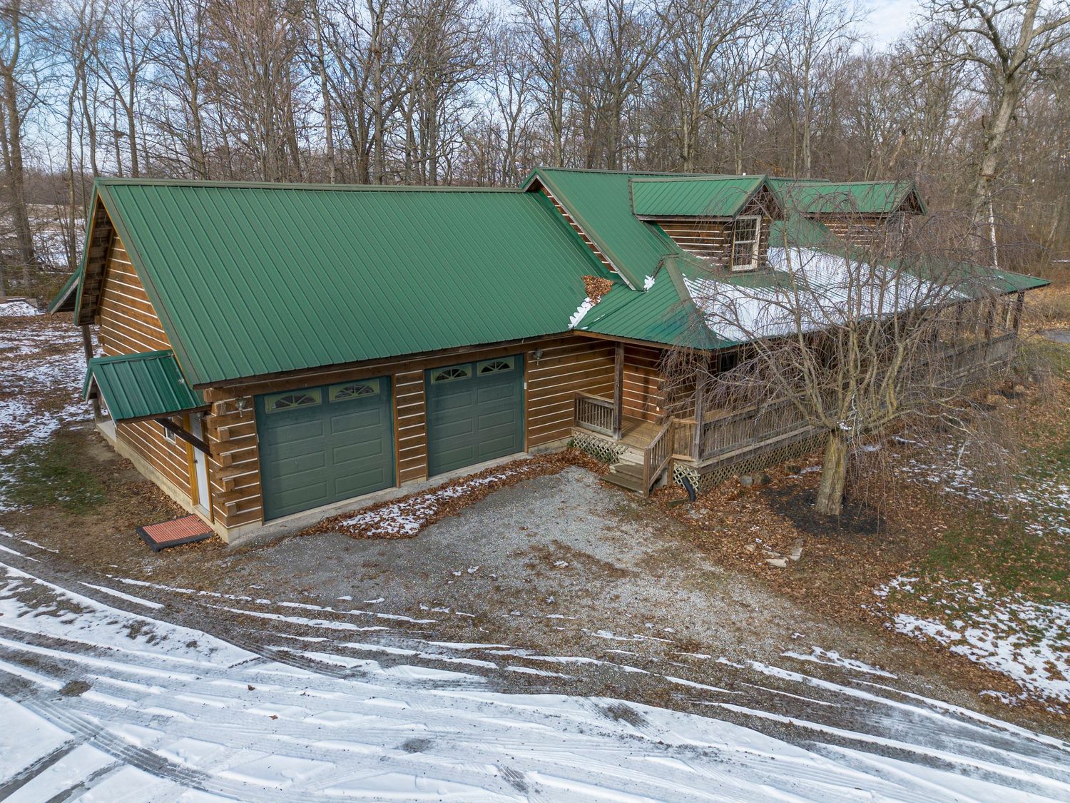 Exterior view of large log cabin structure with green metal roof in winter landscape.