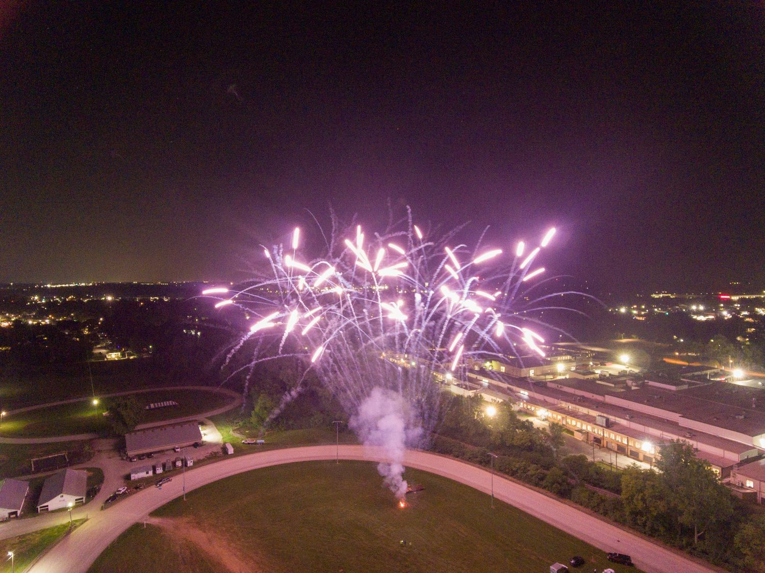 Purple fireworks display bursting over a curved architectural structure at night.