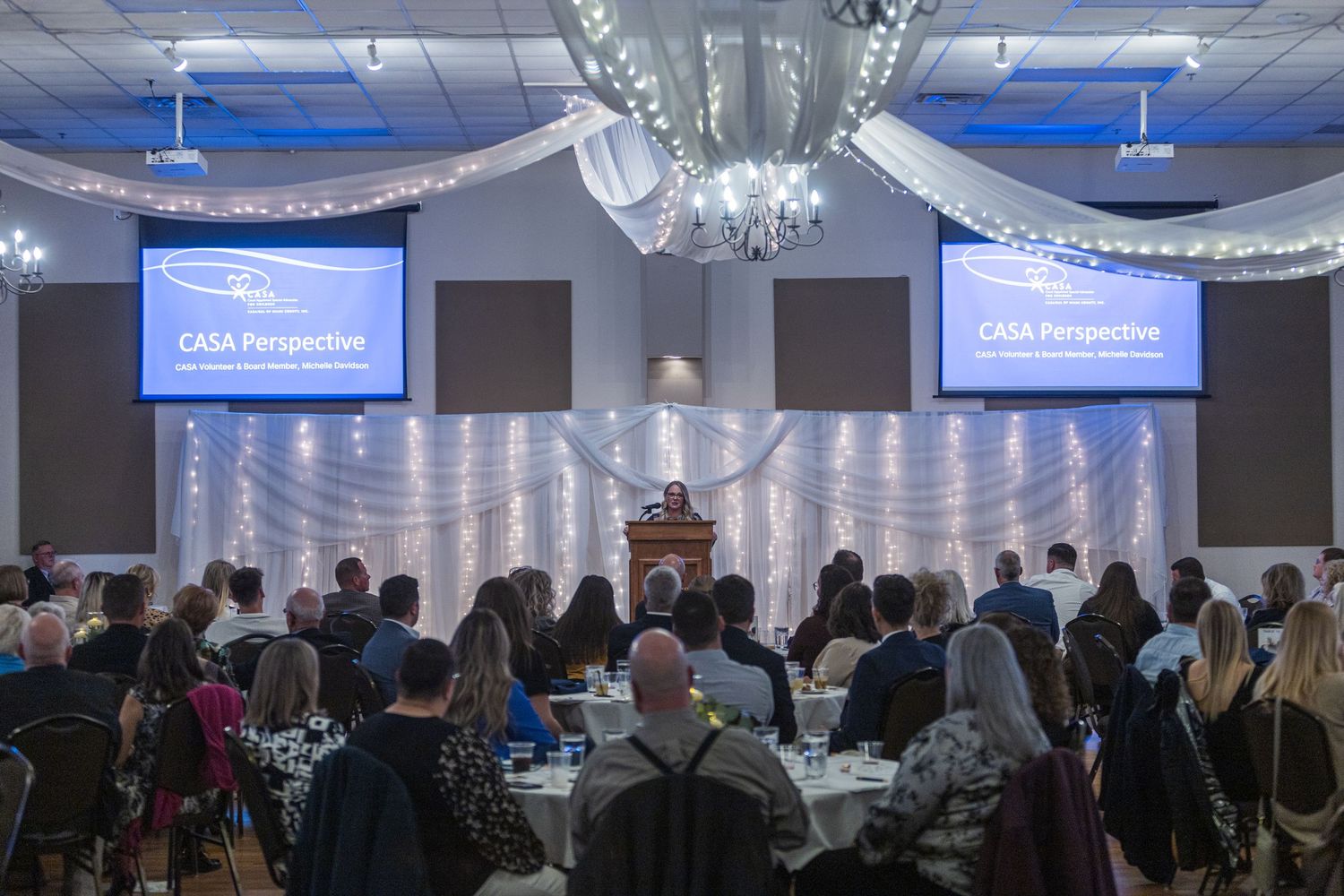 Large indoor event space with blue lighting and rows of tables set up for a gathering.