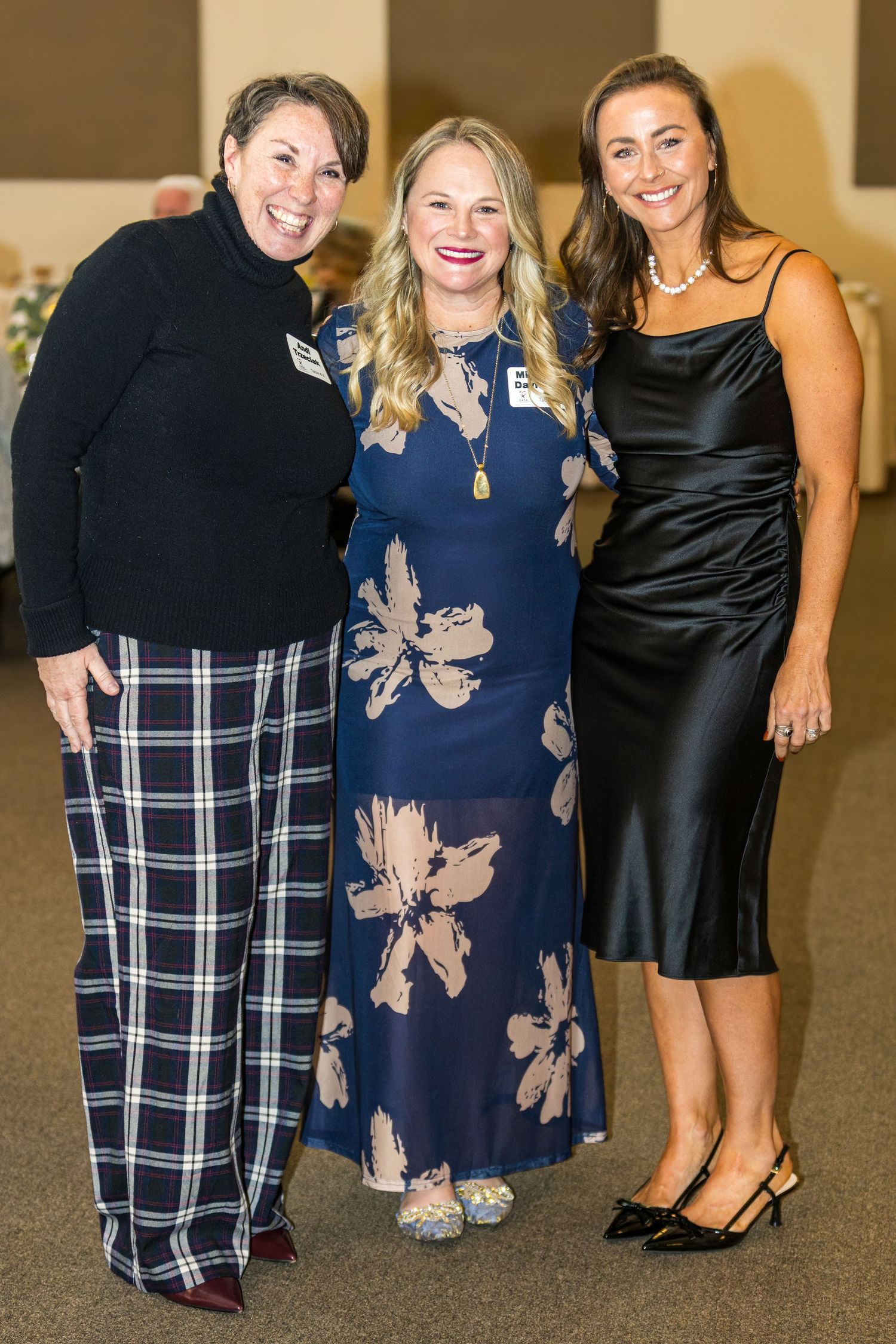 Three women in elegant evening attire pose together at a formal event.