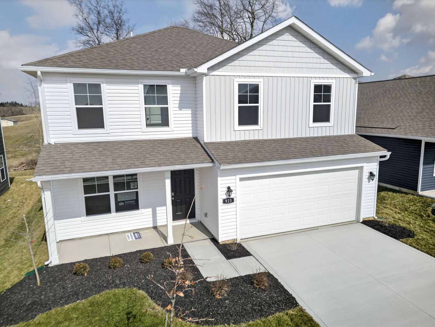 Modern two-story white house with vertical siding, black shutters, and attached two-car garage on new construction lot.