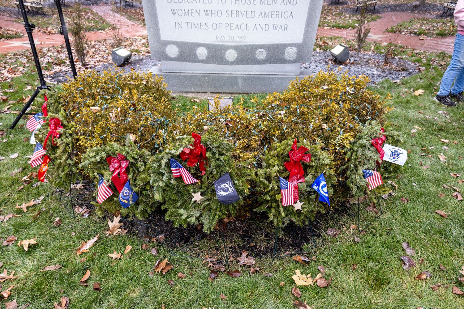 Red and white holiday decorations adorn an outdoor garden area with evergreen shrubs.