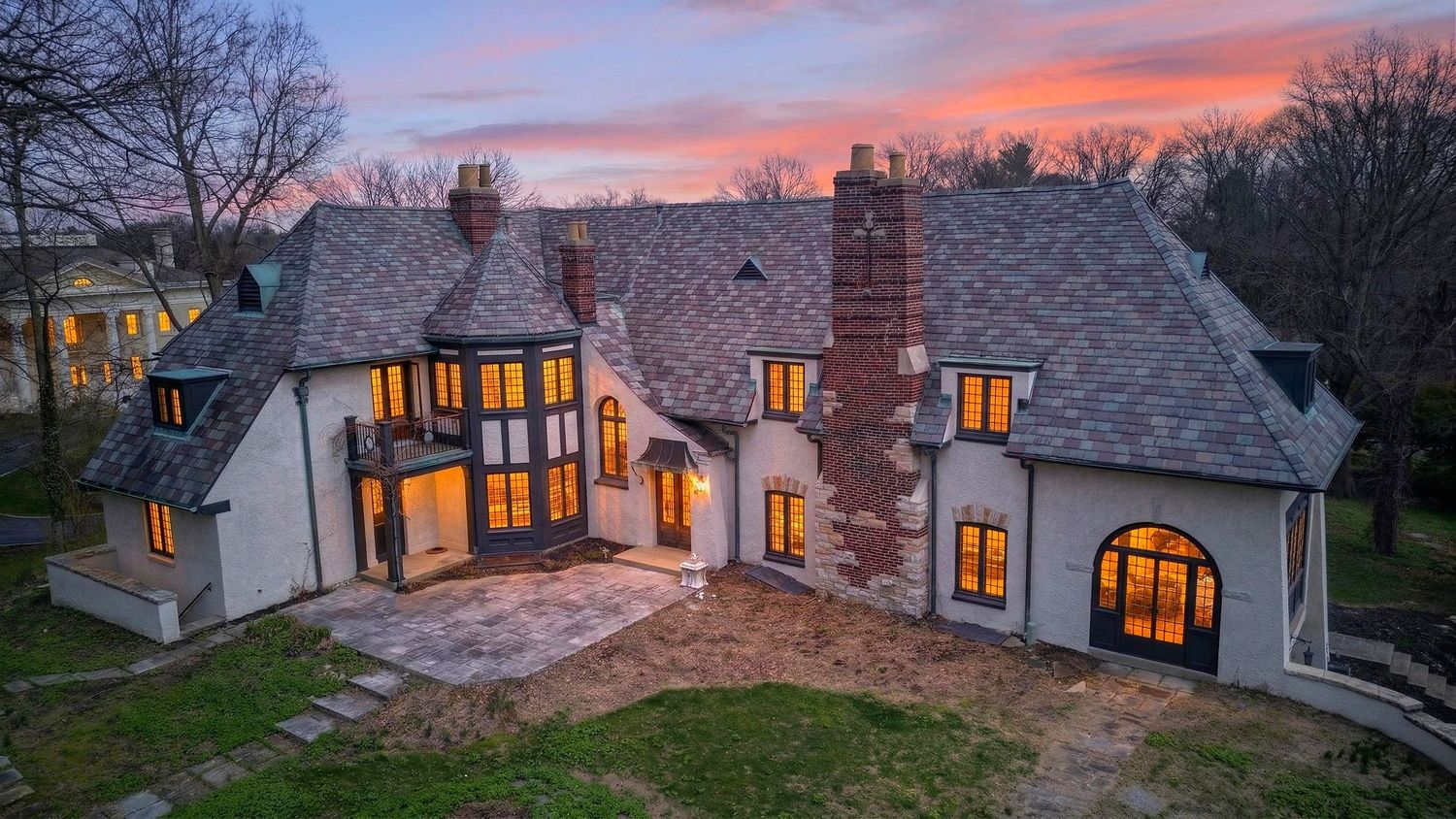 A panoramic sunset view of illuminated cottage windows glowing warmly against a dramatic pink and purple winter sky.