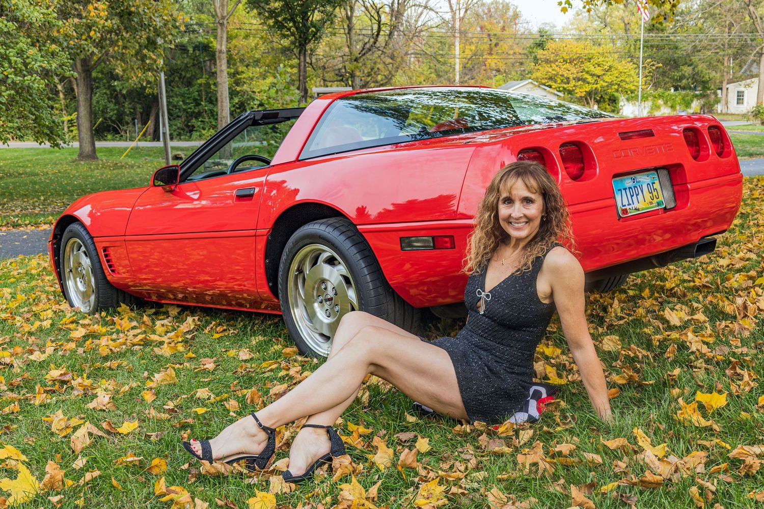 Red sports car parked on autumn leaves with playful poses beside it.