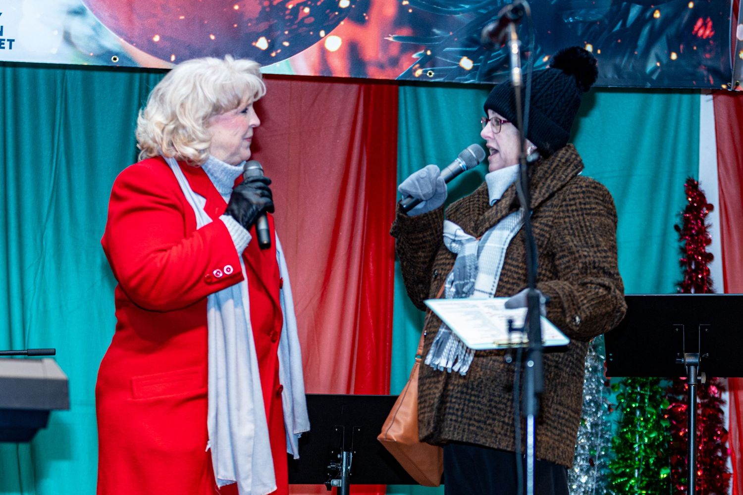 Holiday performers in festive attire on stage with red and turquoise backdrop.