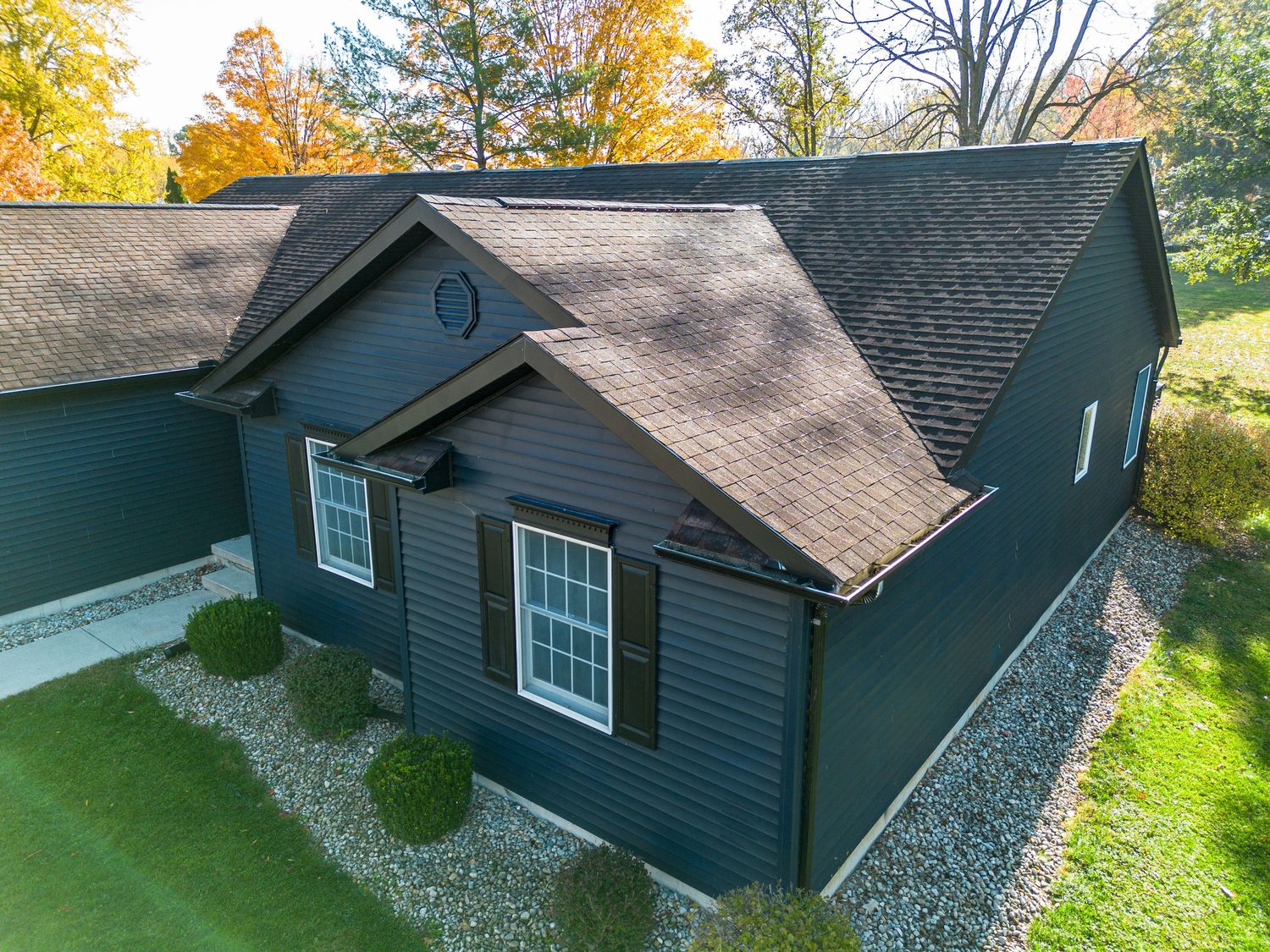 Aerial drone view of a navy blue residential home with a gray roof and landscaping.