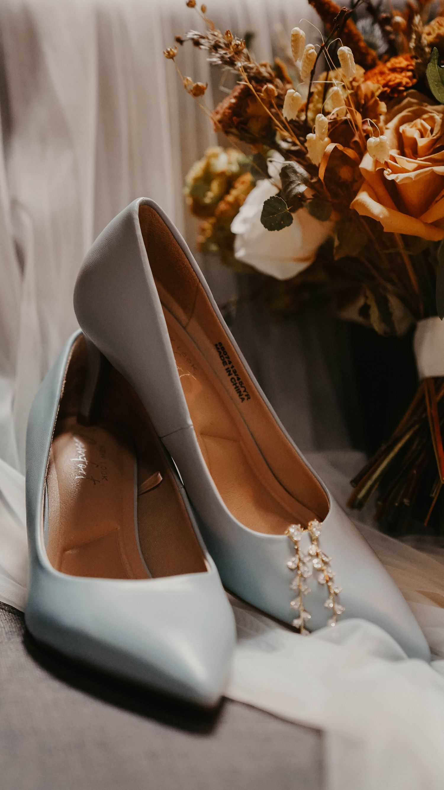Elegant light blue wedding heels displayed with autumn-colored floral decorations in the background.