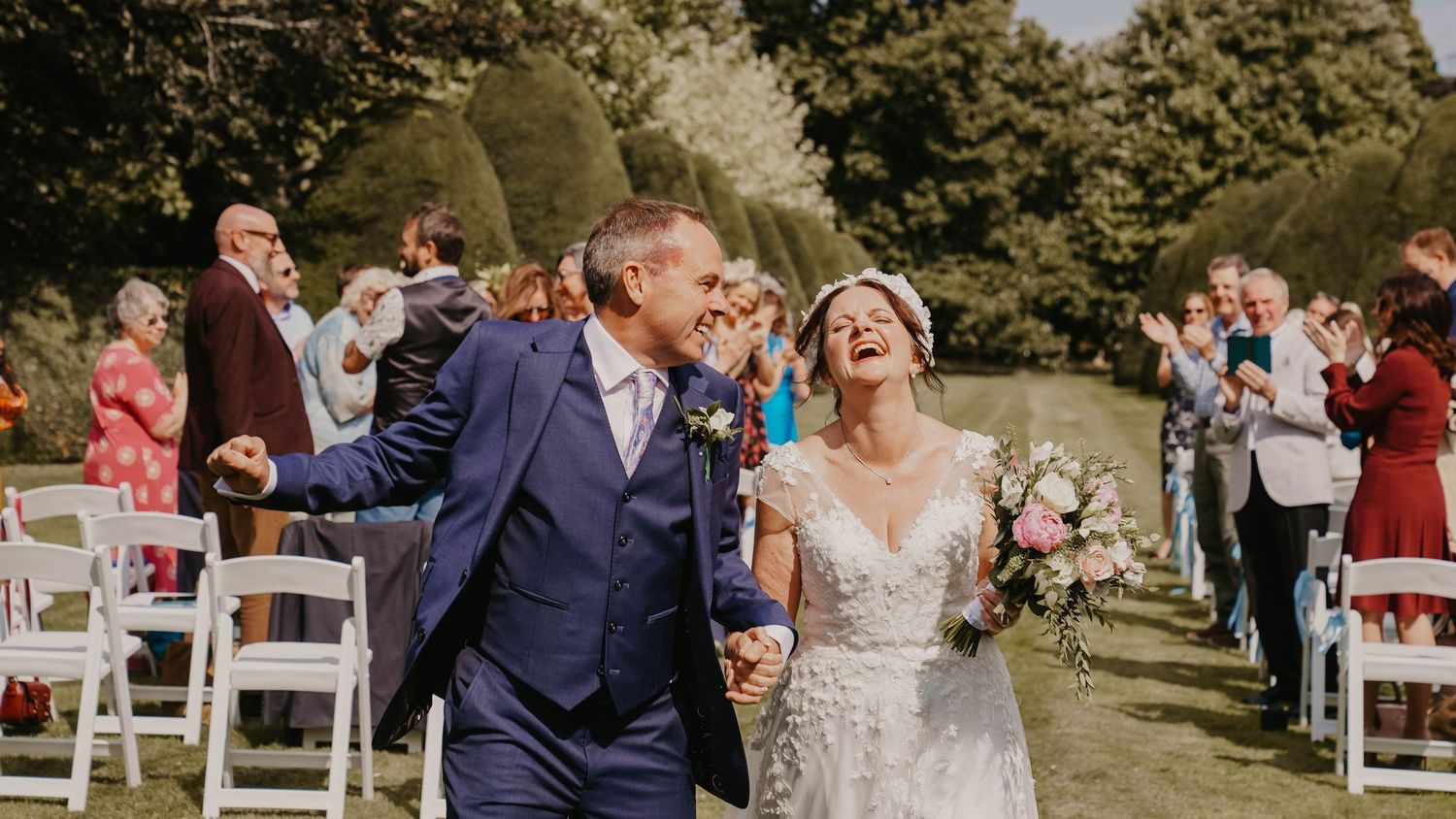 Outdoor wedding ceremony setup with white chairs and natural garden surroundings.