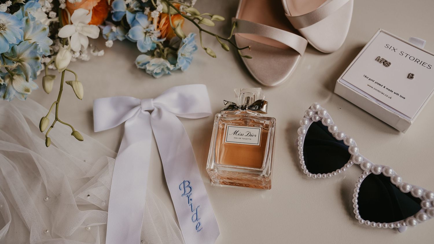 Wedding details including perfume bottles, invitations, and delicate accessories arranged on white surfaces.