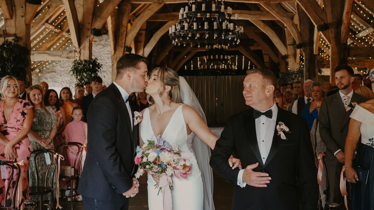 Bride and groom share a tender moment at a rustic barn wedding ceremony, accompanied by father of the bride.