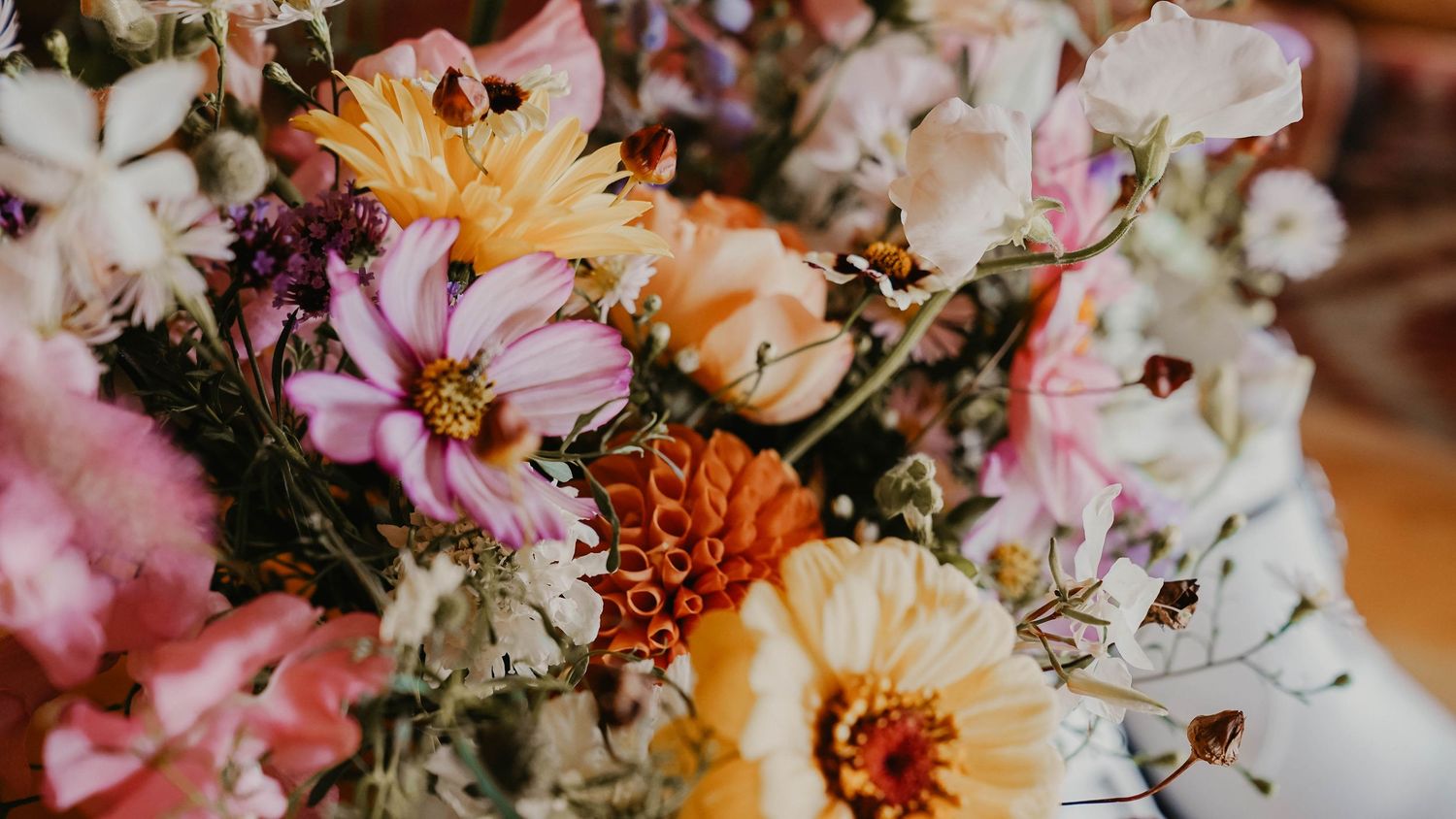 A vibrant bouquet of colorful wildflowers including pink cosmos, orange zinnias, and white blooms arranged together.