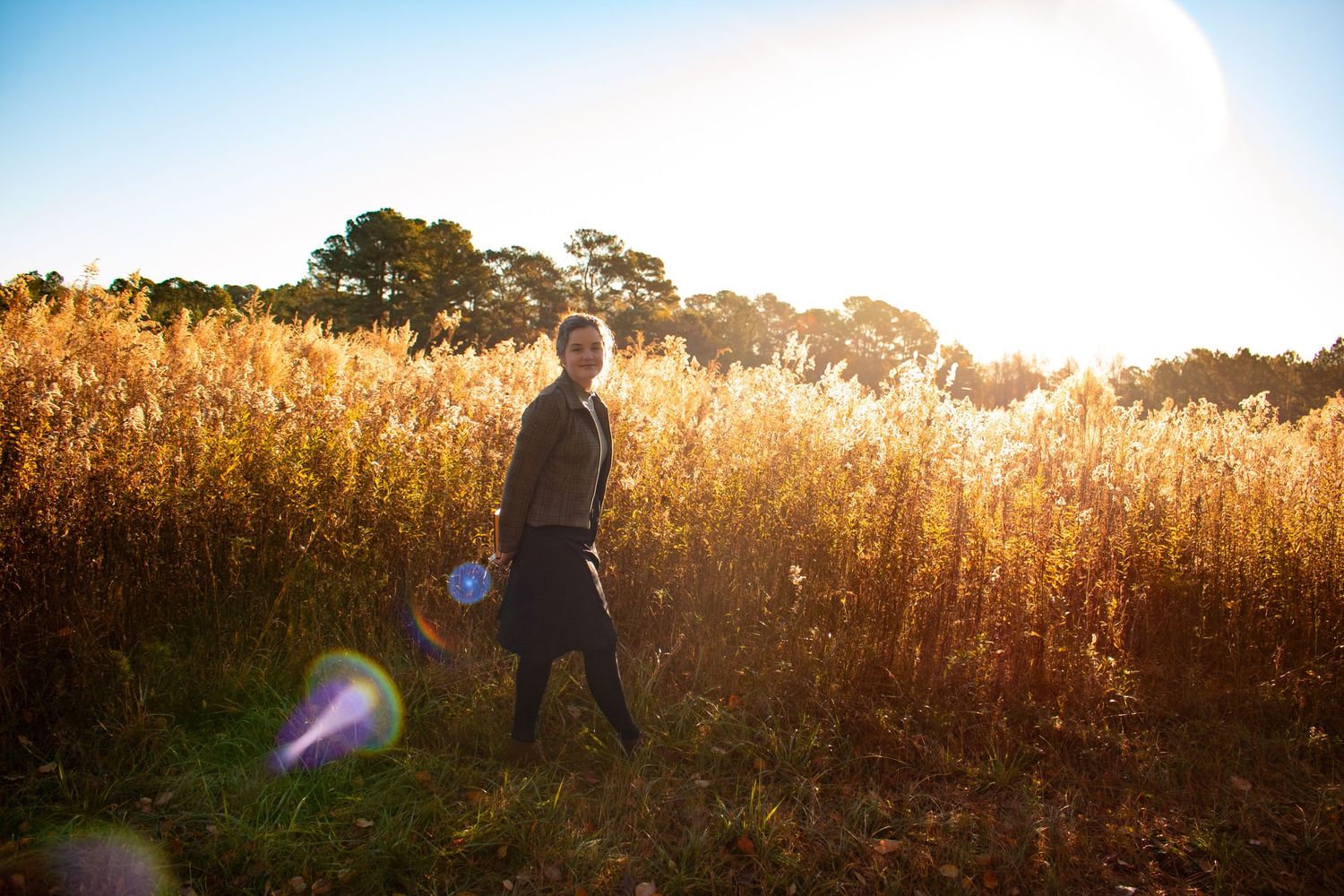 Person walking through golden sunlit field with tall grass and trees in warm autumn light.