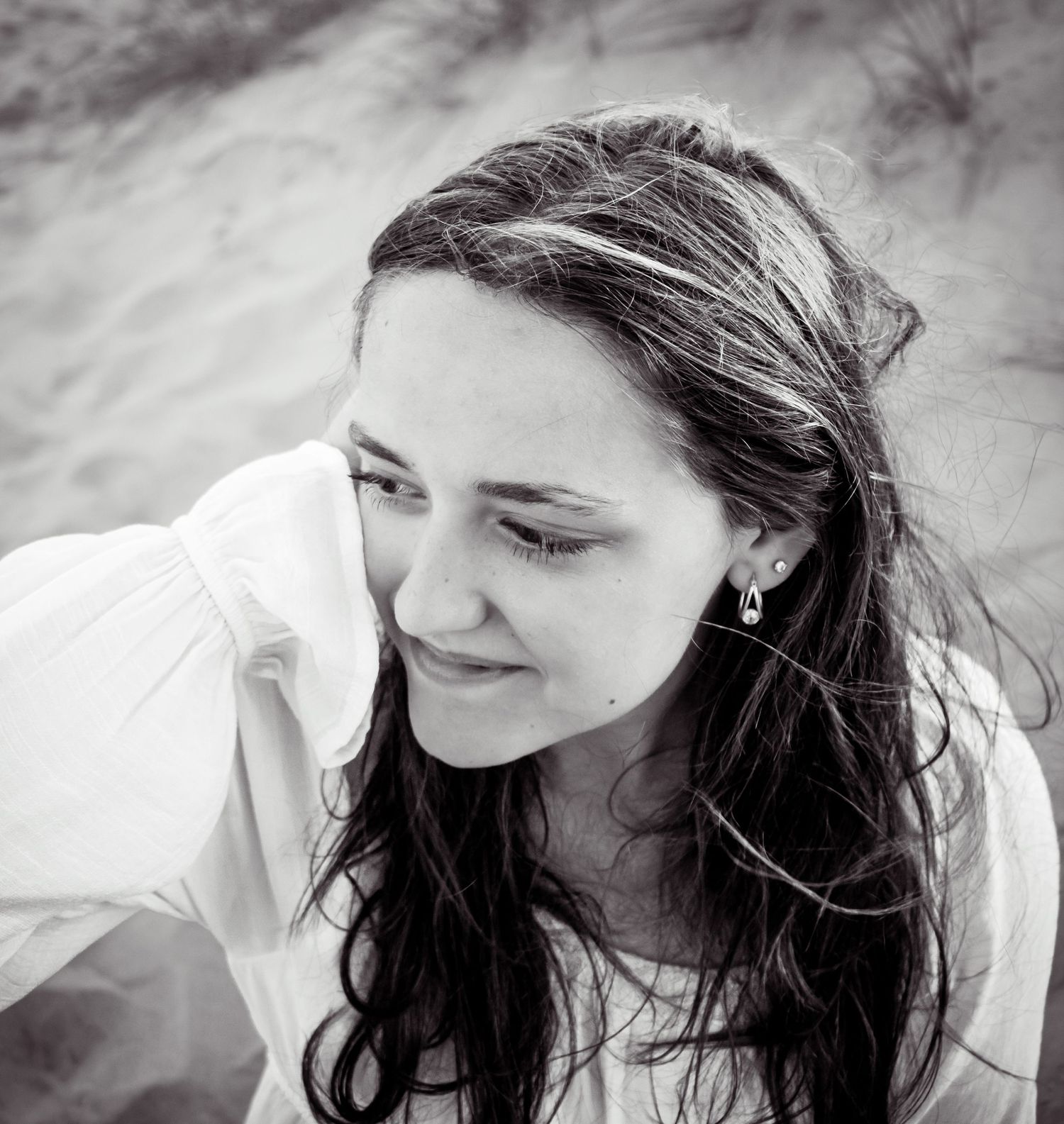 Black and white portrait of a person with long dark hair smiling while looking down in natural light.