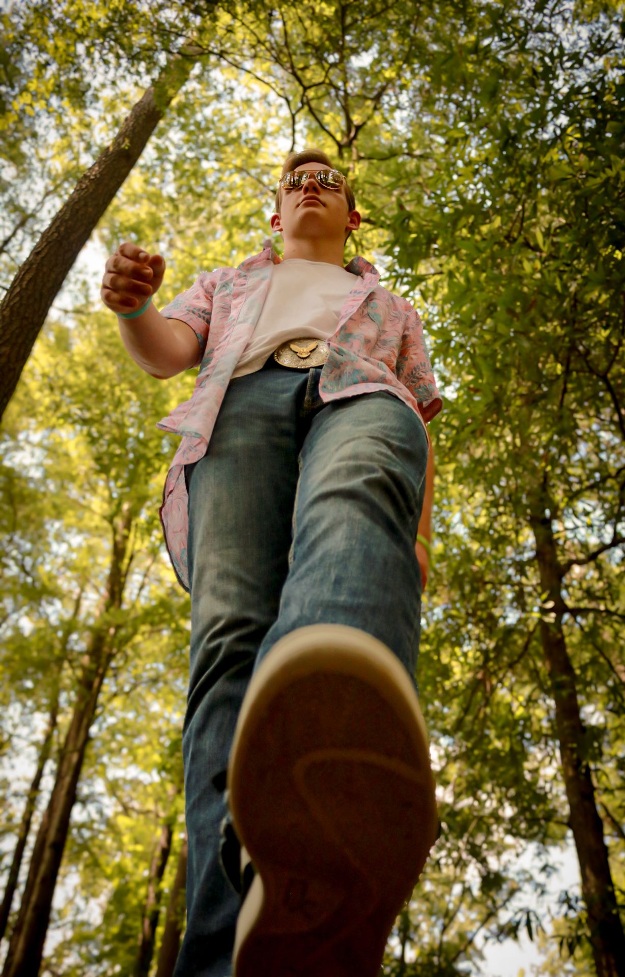 Low angle view of someone in sunglasses and pink jacket standing in a forest with trees towering overhead.