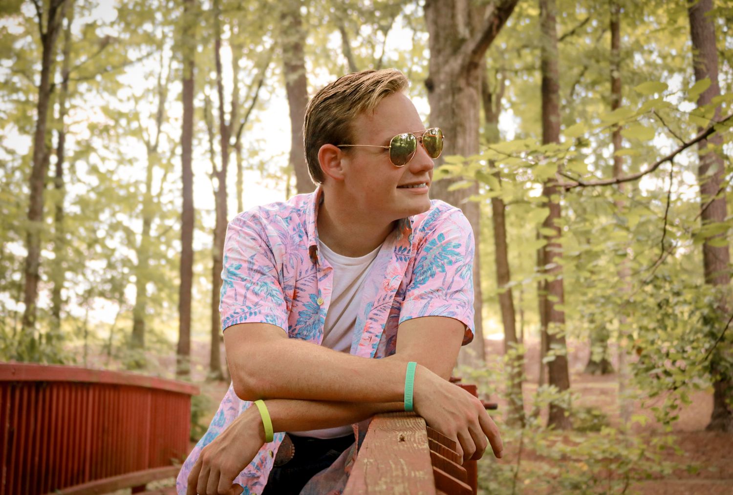 Person in pink floral shirt sits outdoors in wooded area during daytime.
