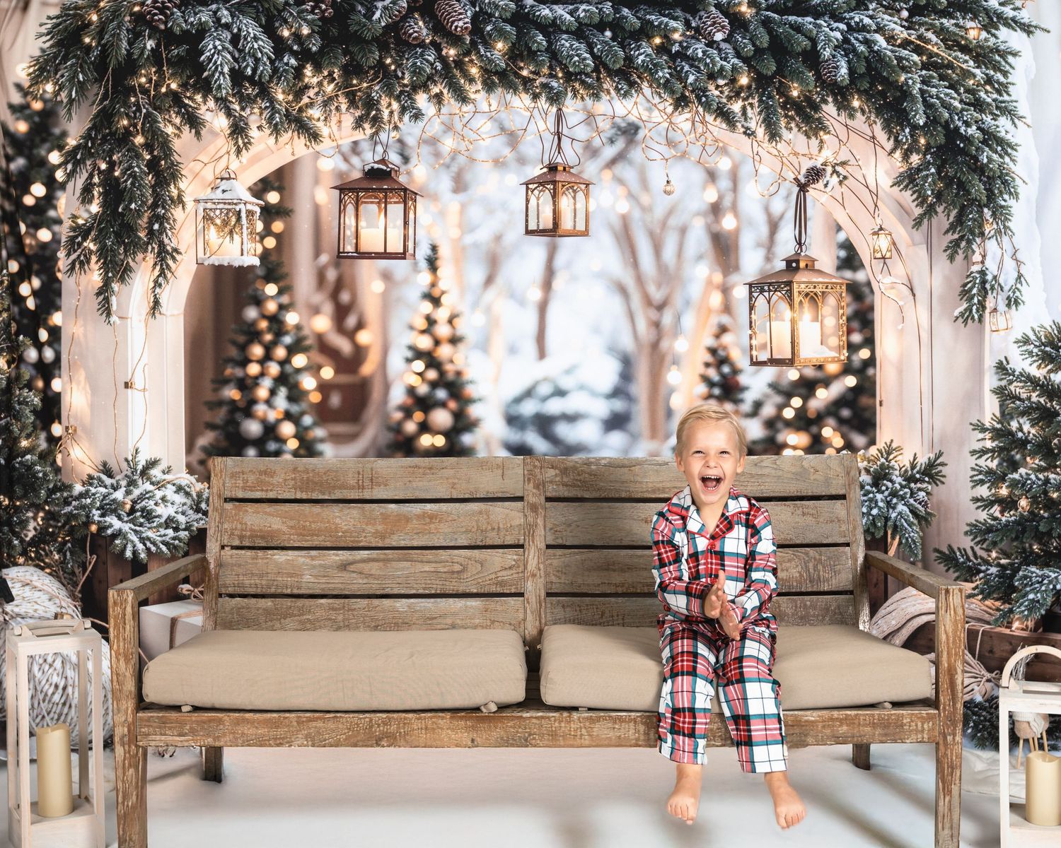 A rustic wooden bench sits beneath snow-covered evergreen branches with twinkling lights and lanterns creating a cozy winter scene.
