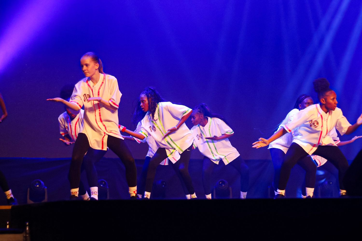 Dancers in white costumes perform choreographed routine under blue lighting.