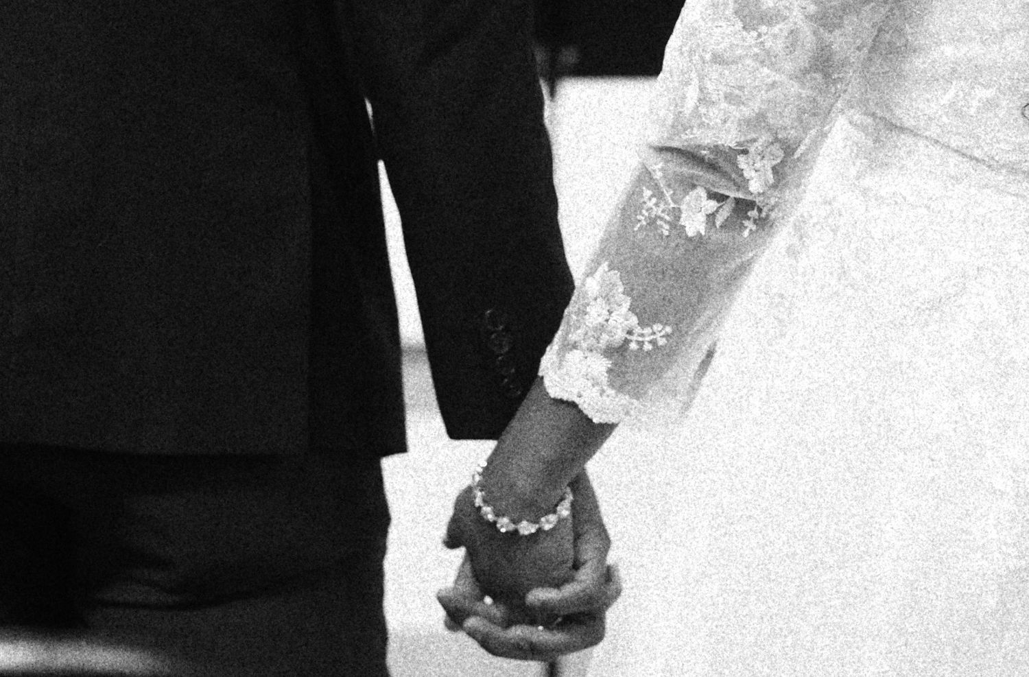 Close-up of hands holding in formal wedding attire.