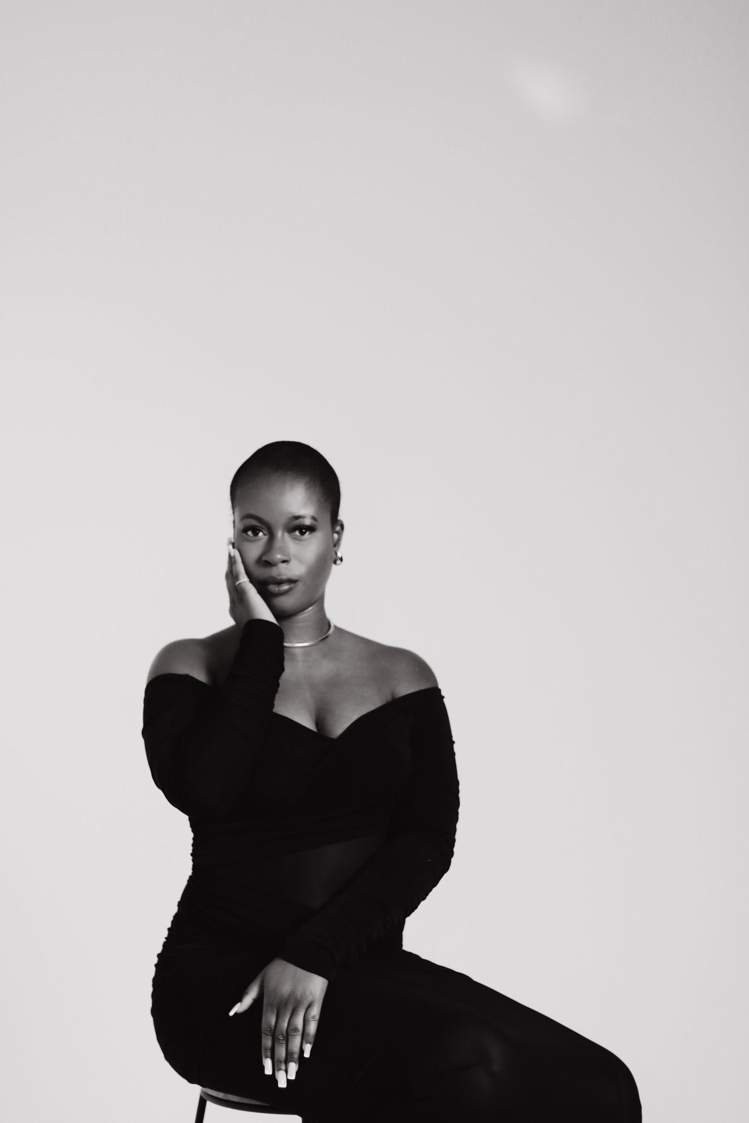 Black and white portrait of a woman in an off-shoulder black gown seated gracefully against a light background.