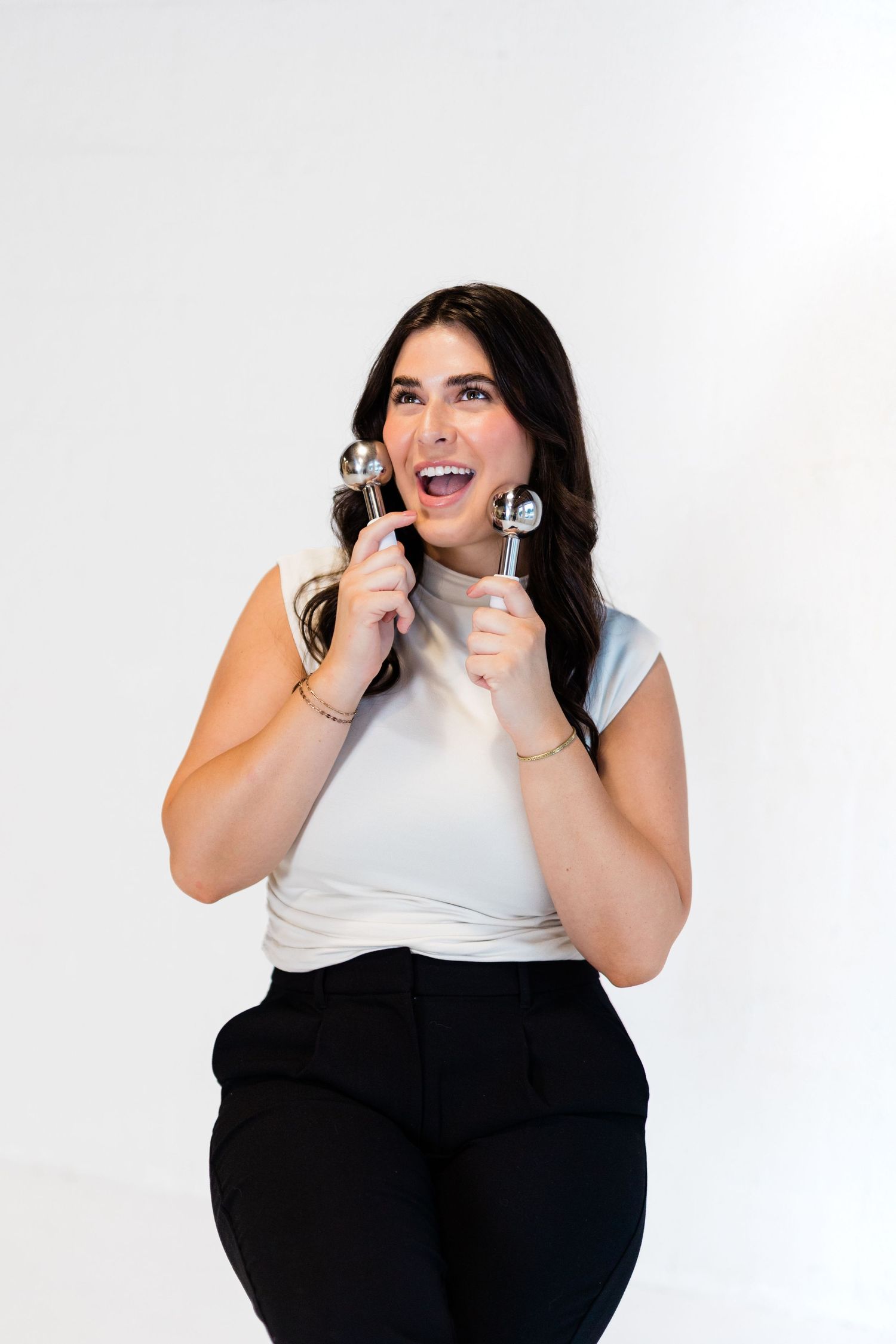 Woman in casual attire holds microphone while singing against white background.