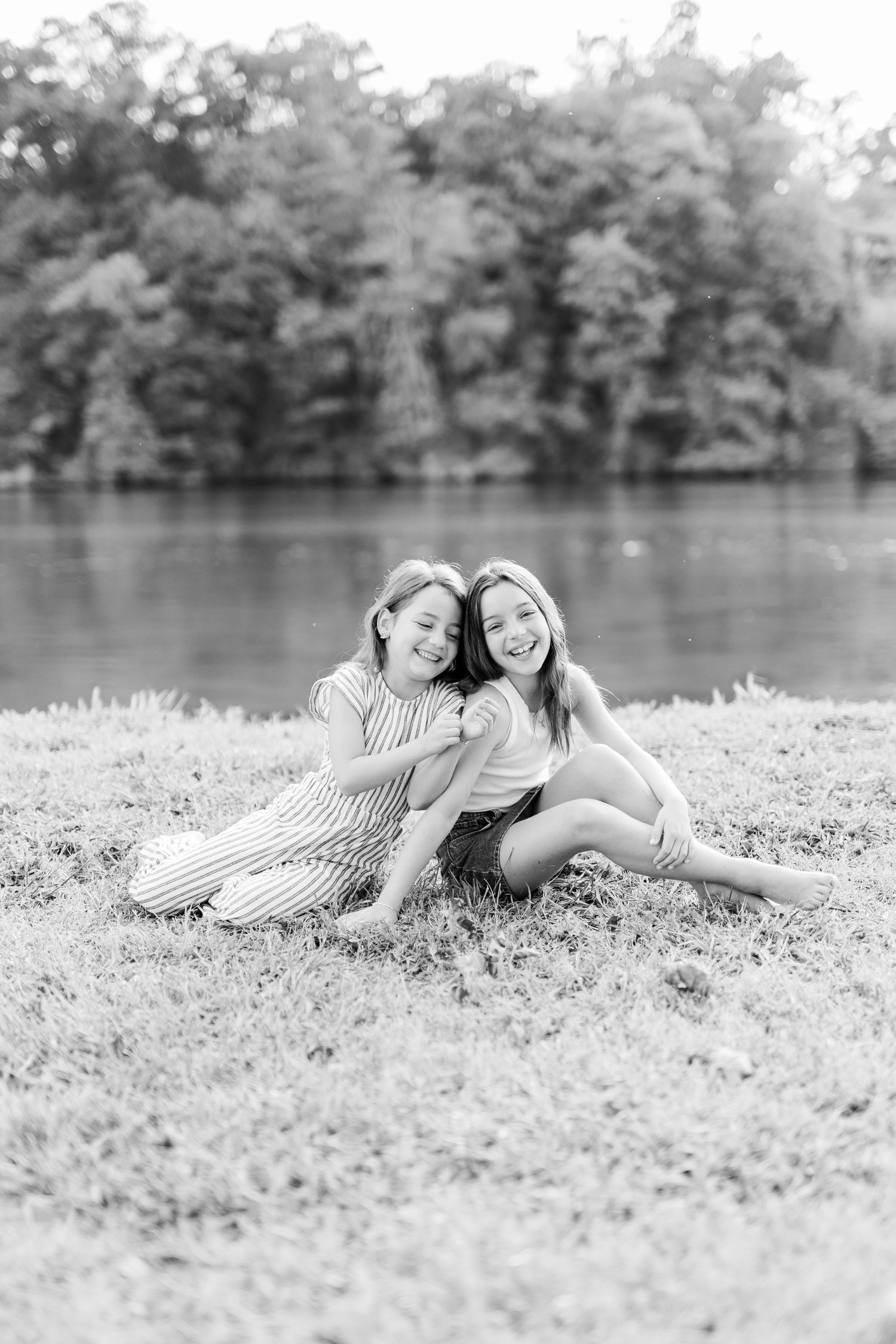 Black and white portrait of two friends sitting together by lake, sharing laughter.