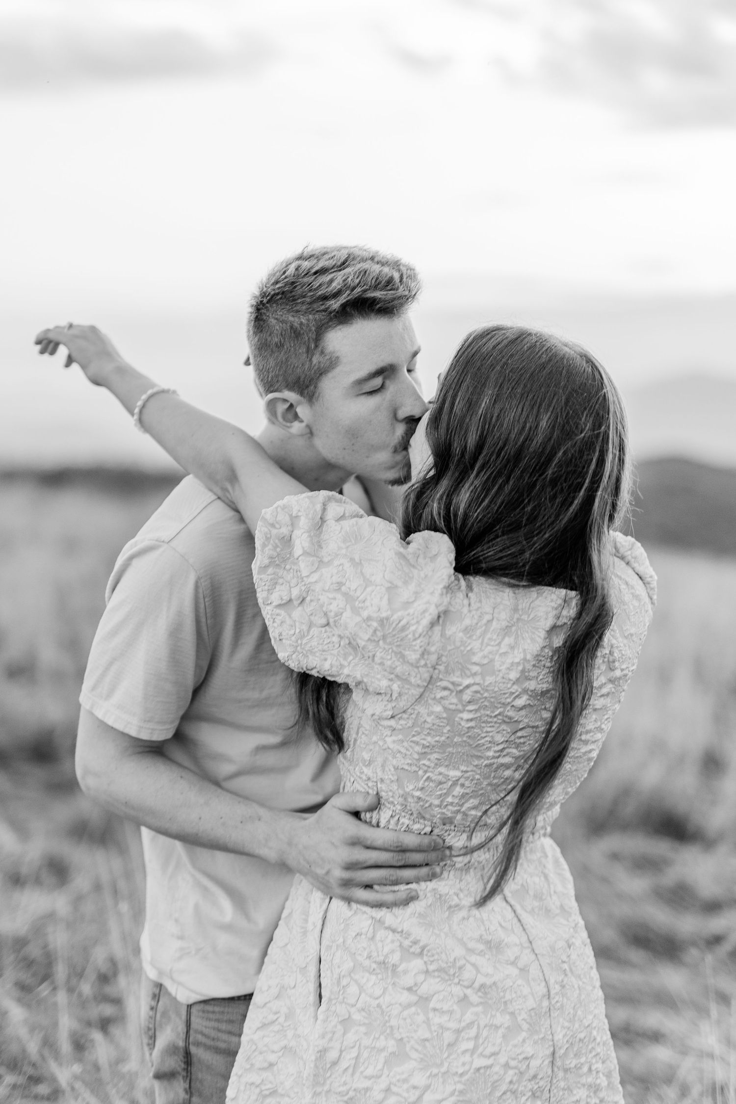 A romantic embrace between two people in a field during golden hour.