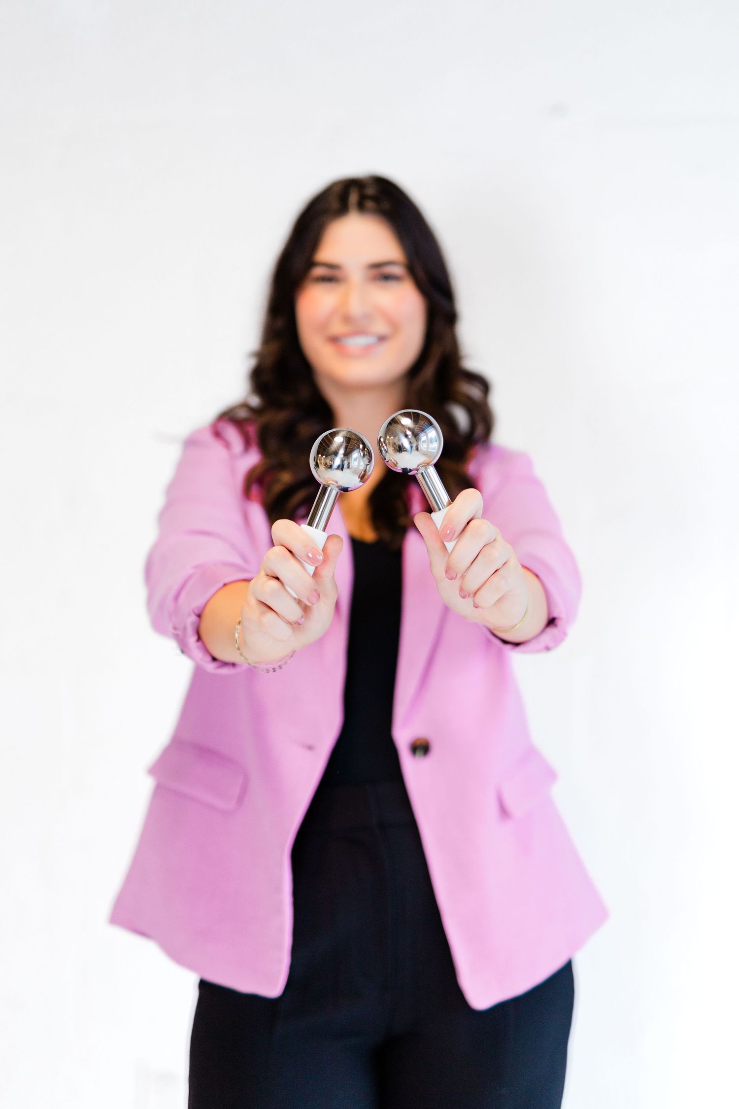 Professional in pink blazer holding up two measurement tools against white background.