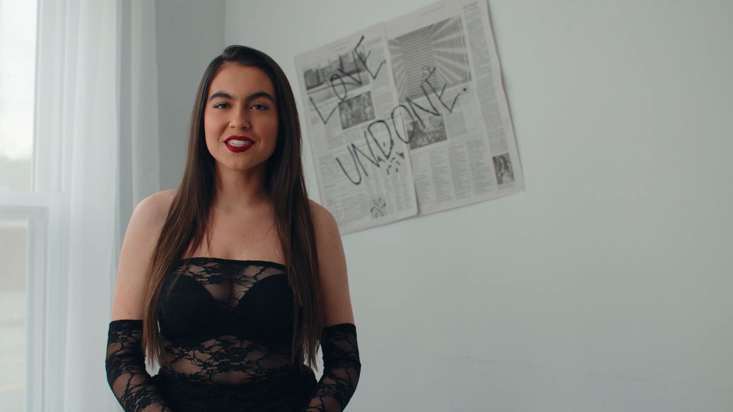A person in black attire stands against a white wall in a modern interior setting.