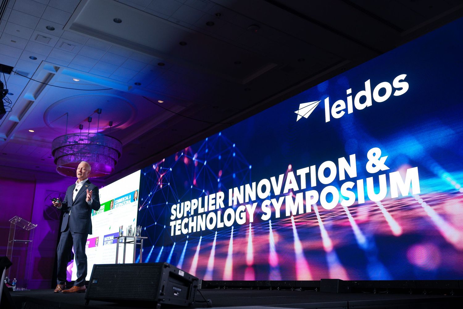 Corporate event stage setup with blue lighting and digital displays showing company branding and presentation content.