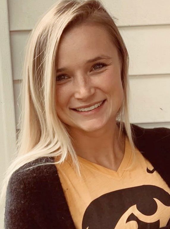 Someone wearing a yellow and black University of Iowa Hawkeyes shirt smiles at the camera.