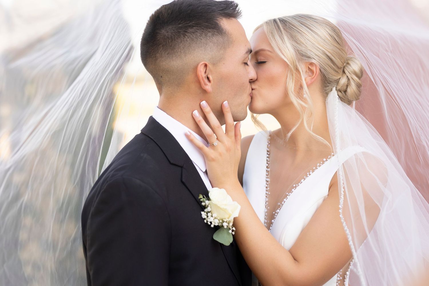 Newlywed couple shares a romantic kiss under a flowing white veil on their wedding day.