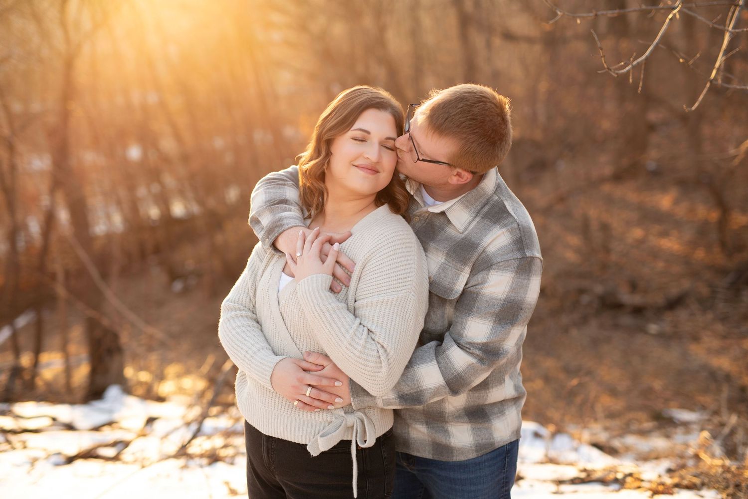 A couple embraces outdoors during golden hour in autumn with sunlight filtering through trees in the background.