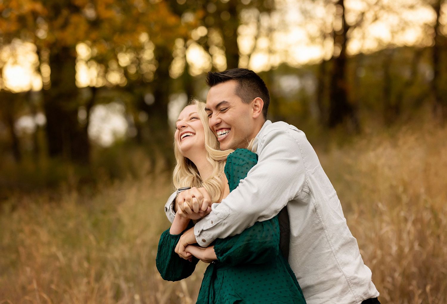 A couple laughs together while embracing in a golden autumn field at sunset.